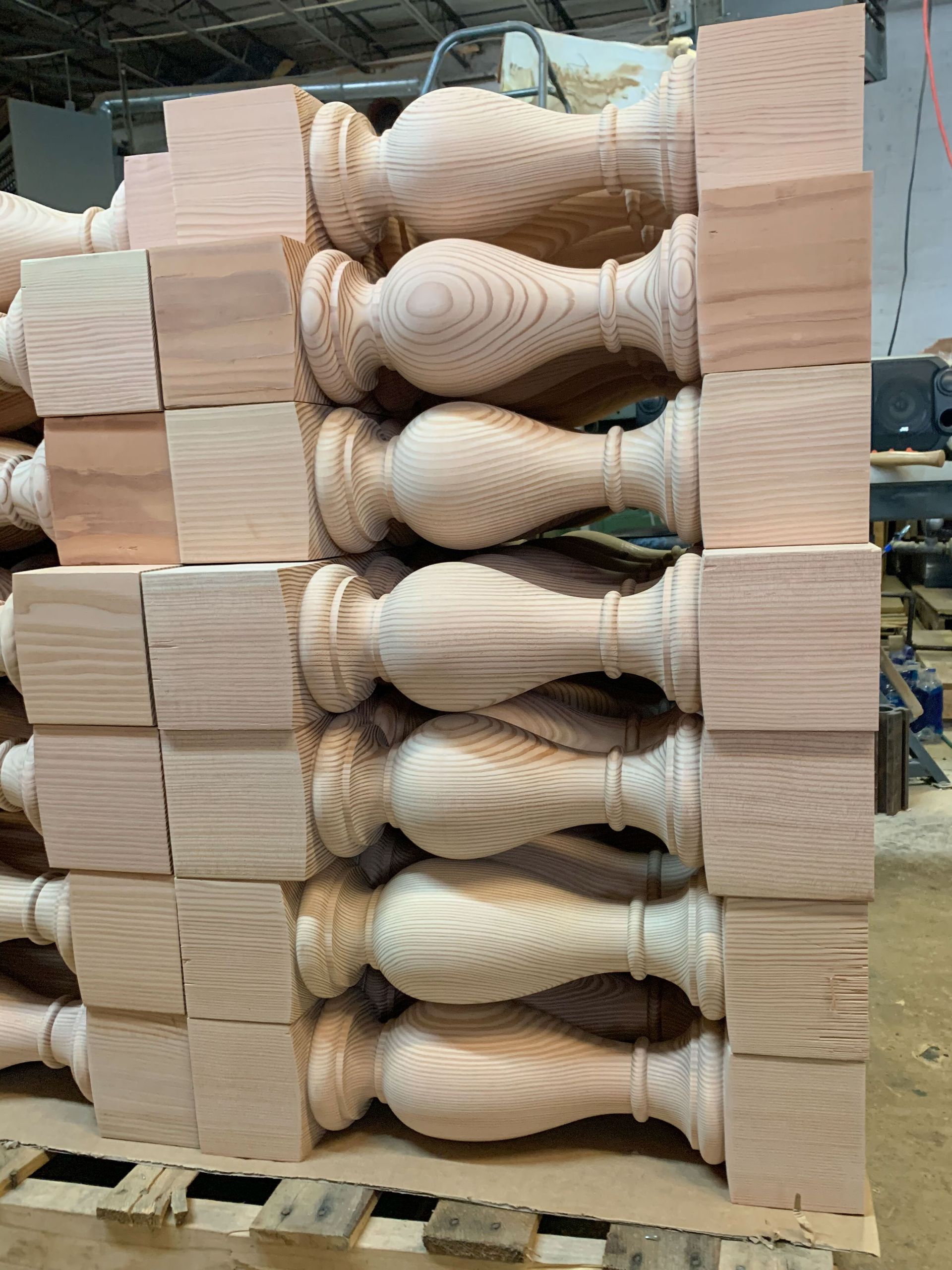 Stack of unfinished wooden balusters and square blocks on a pallet in a workshop.