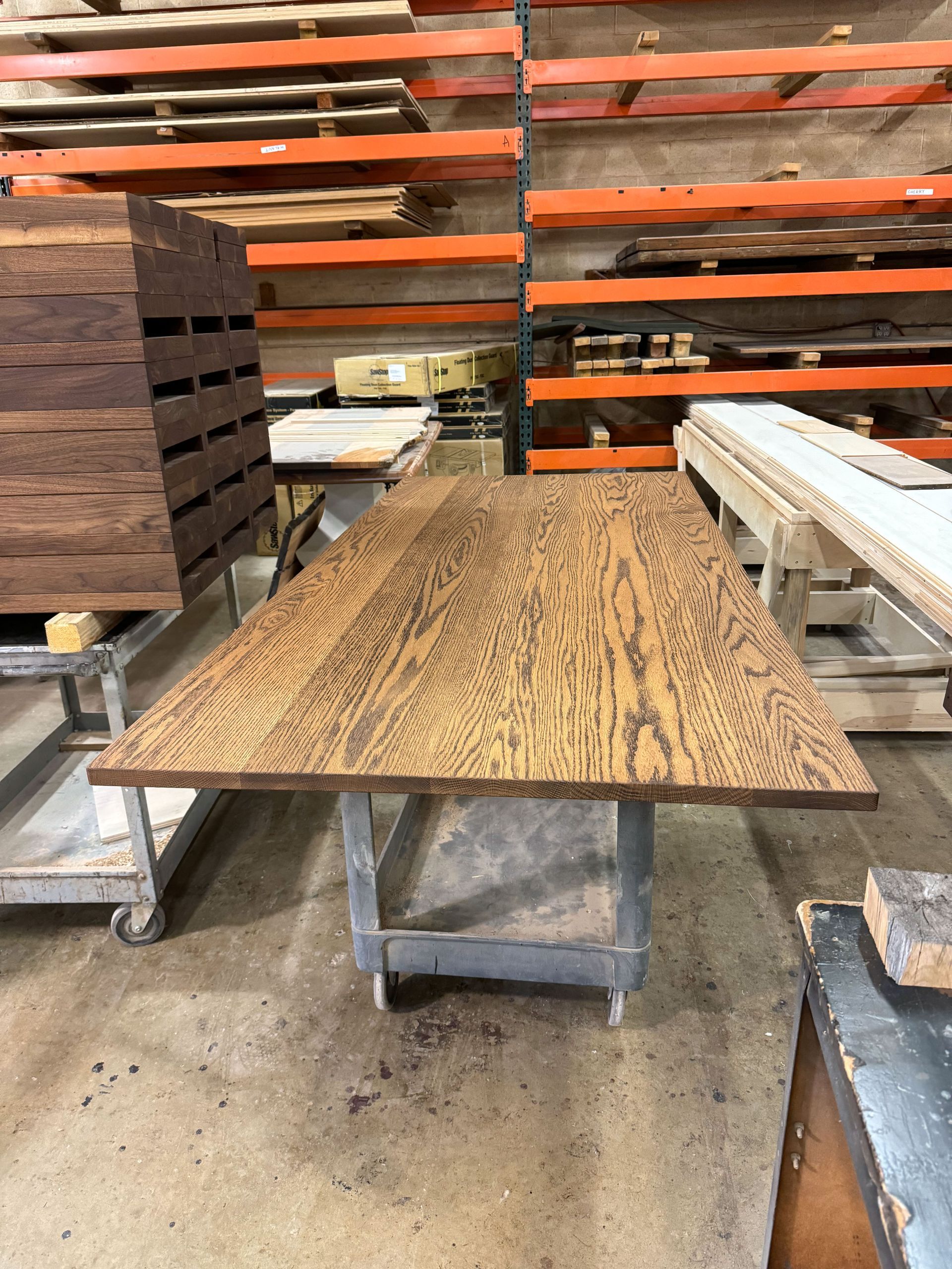 Wood table with unique grain pattern, sits on metal frame in a wood shop. Shelves of lumber are in the background.