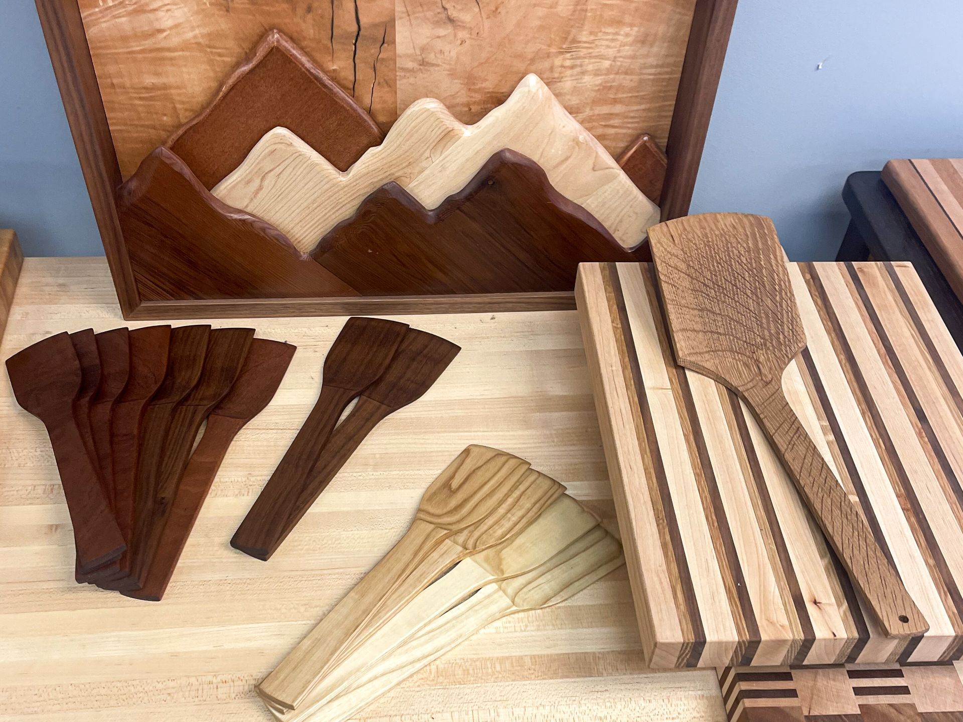 Wooden art and kitchen tools: Mountain scene, spatulas, cutting boards in various wood tones.