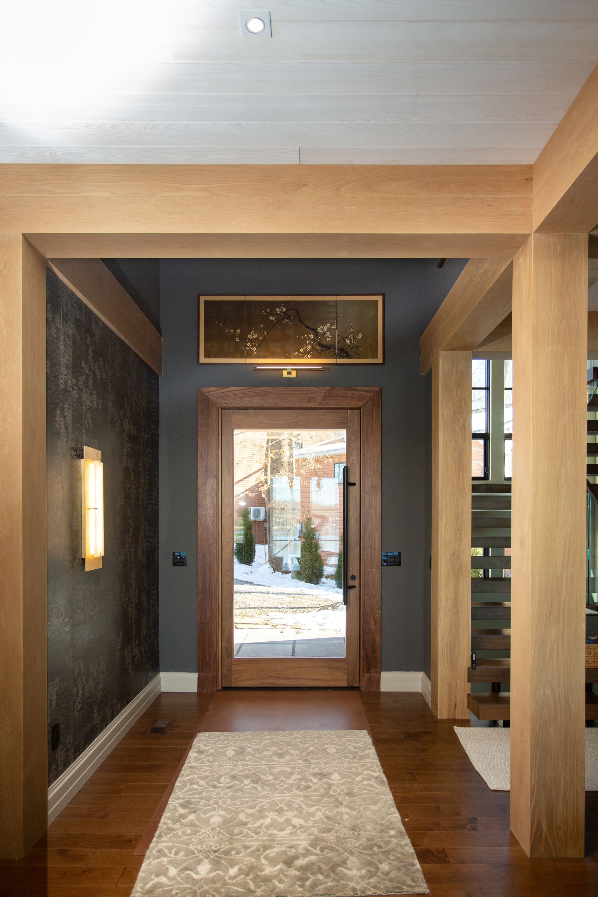 Wooden entryway with a glass door, artwork, dark gray walls, and light beige beams.