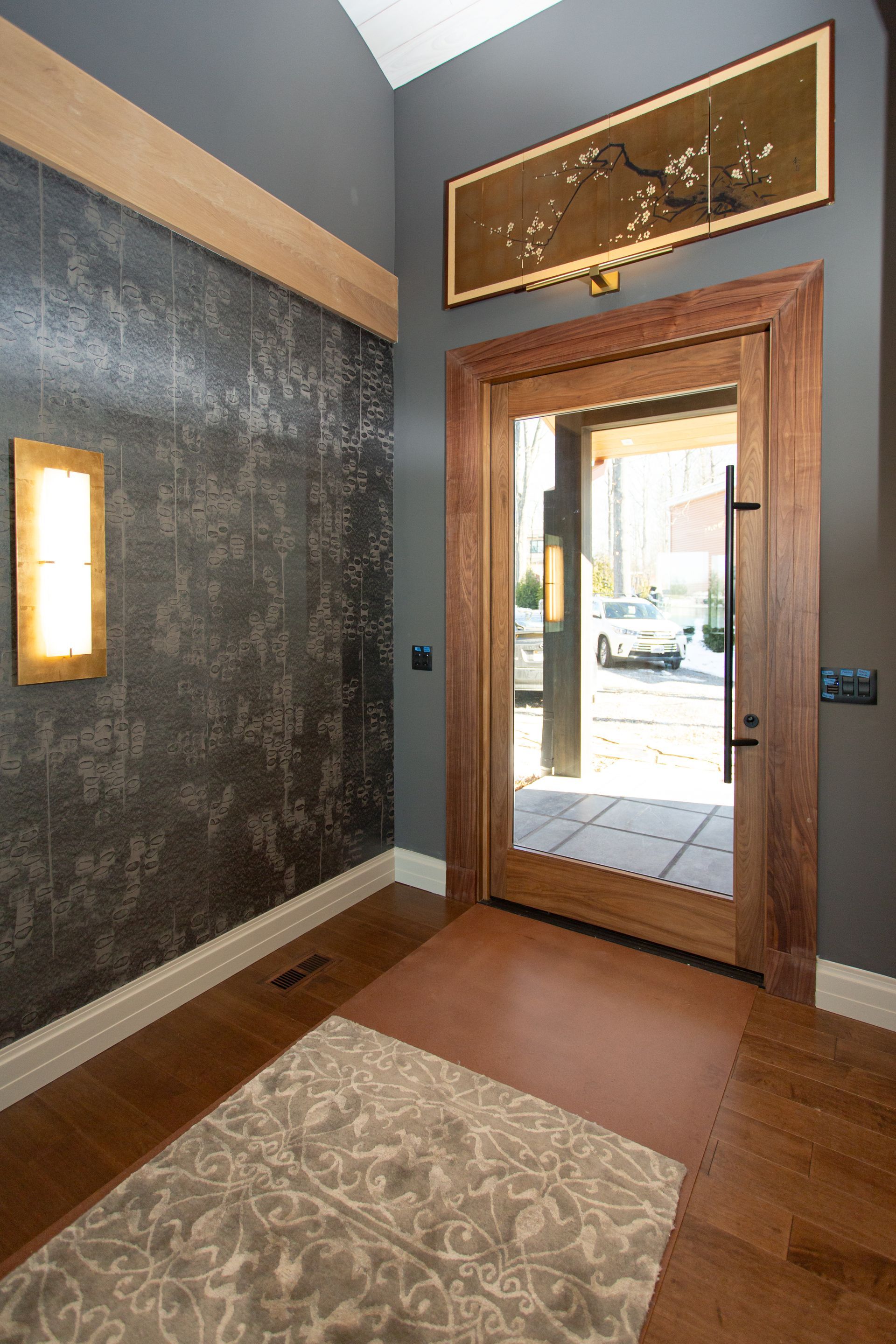 Entryway with wooden door, dark accent wall, artwork, and area rug.
