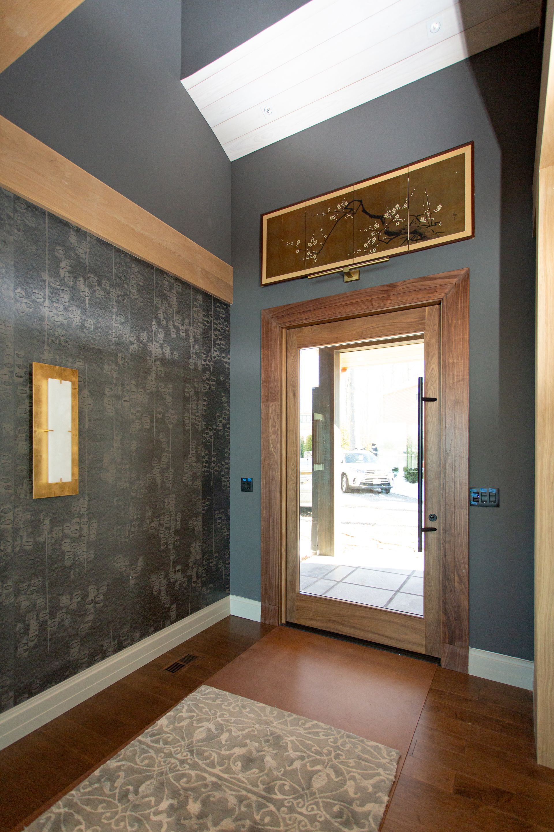 Entryway with gray walls, wooden door and trim, art, and patterned rug.