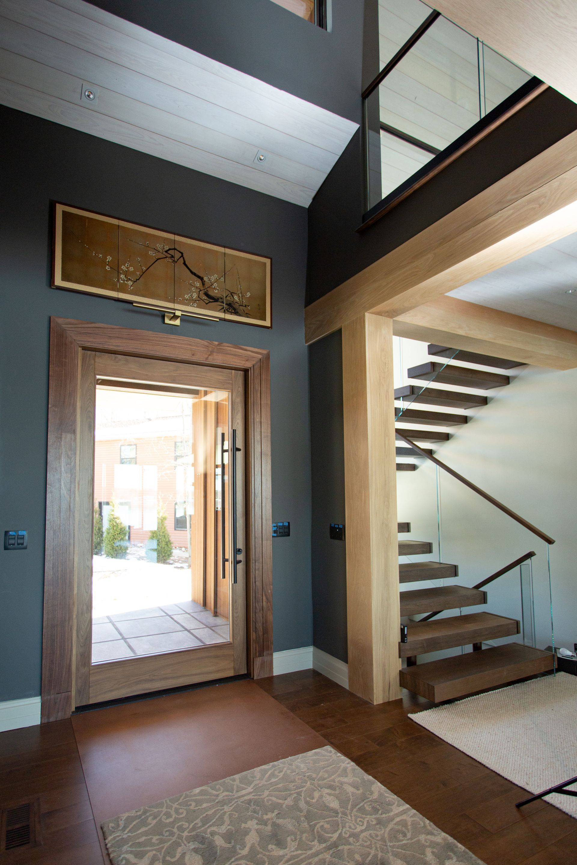 Entryway with dark gray walls, wooden door and stairs, gold artwork.