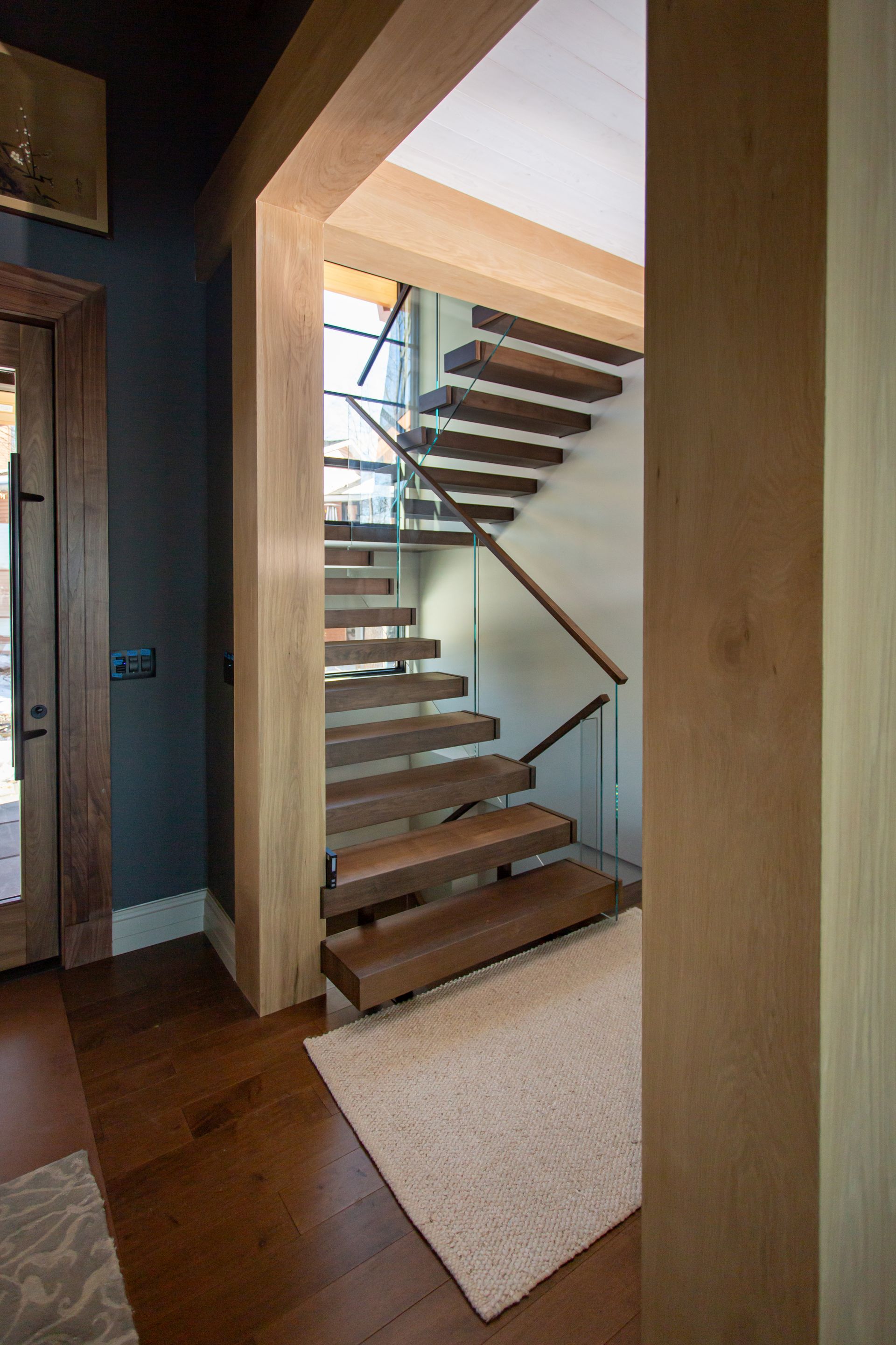 Wooden staircase in a home with glass railing, and wood flooring.