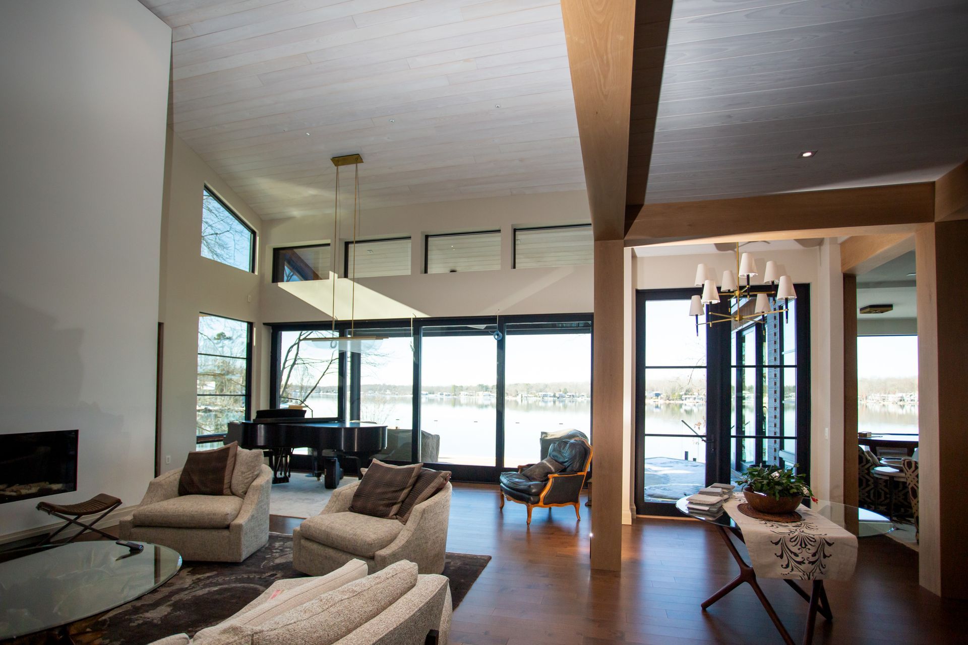 Spacious living room with large windows, piano, and armchairs overlooking a lake.
