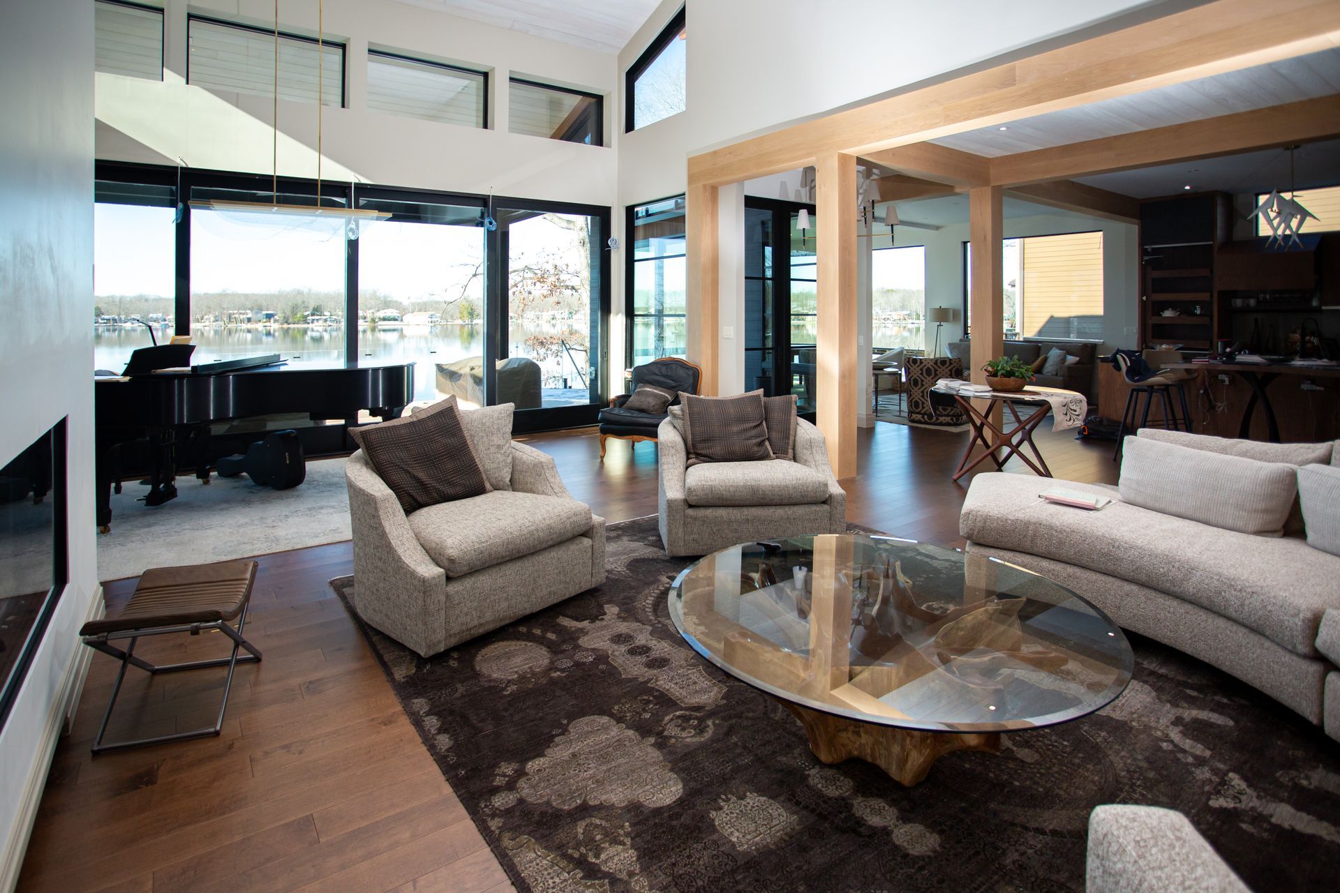 Modern living room with lake view, featuring seating, grand piano, and large windows.