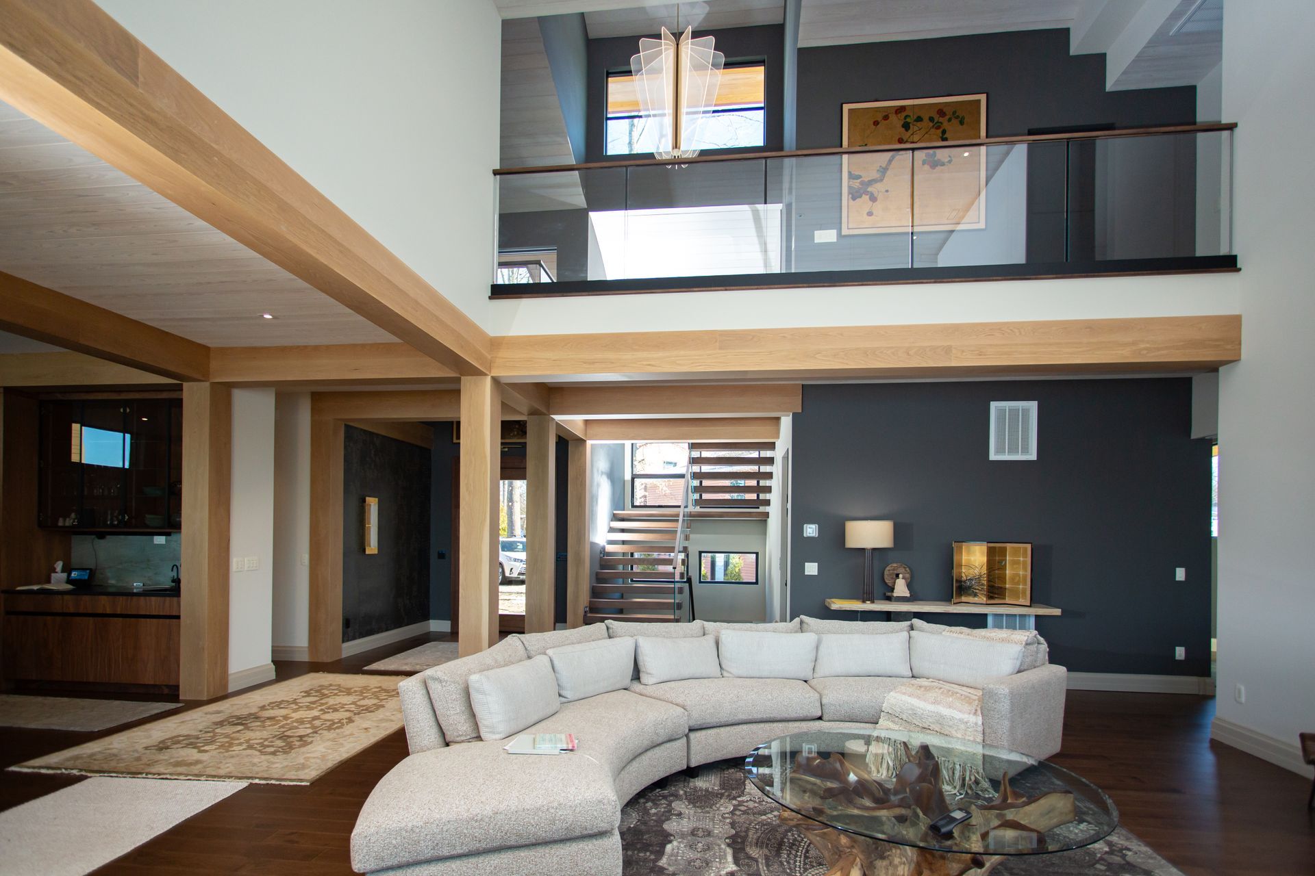 Modern living room with curved sofa, glass coffee table, and mezzanine overlooking the space.