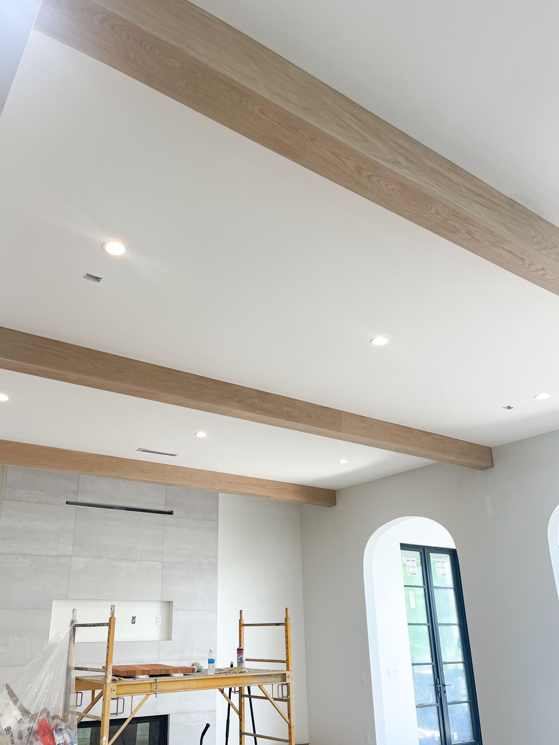 Interior ceiling with light-colored beams, recessed lights, and a white fireplace. Arched doorway with black frame.