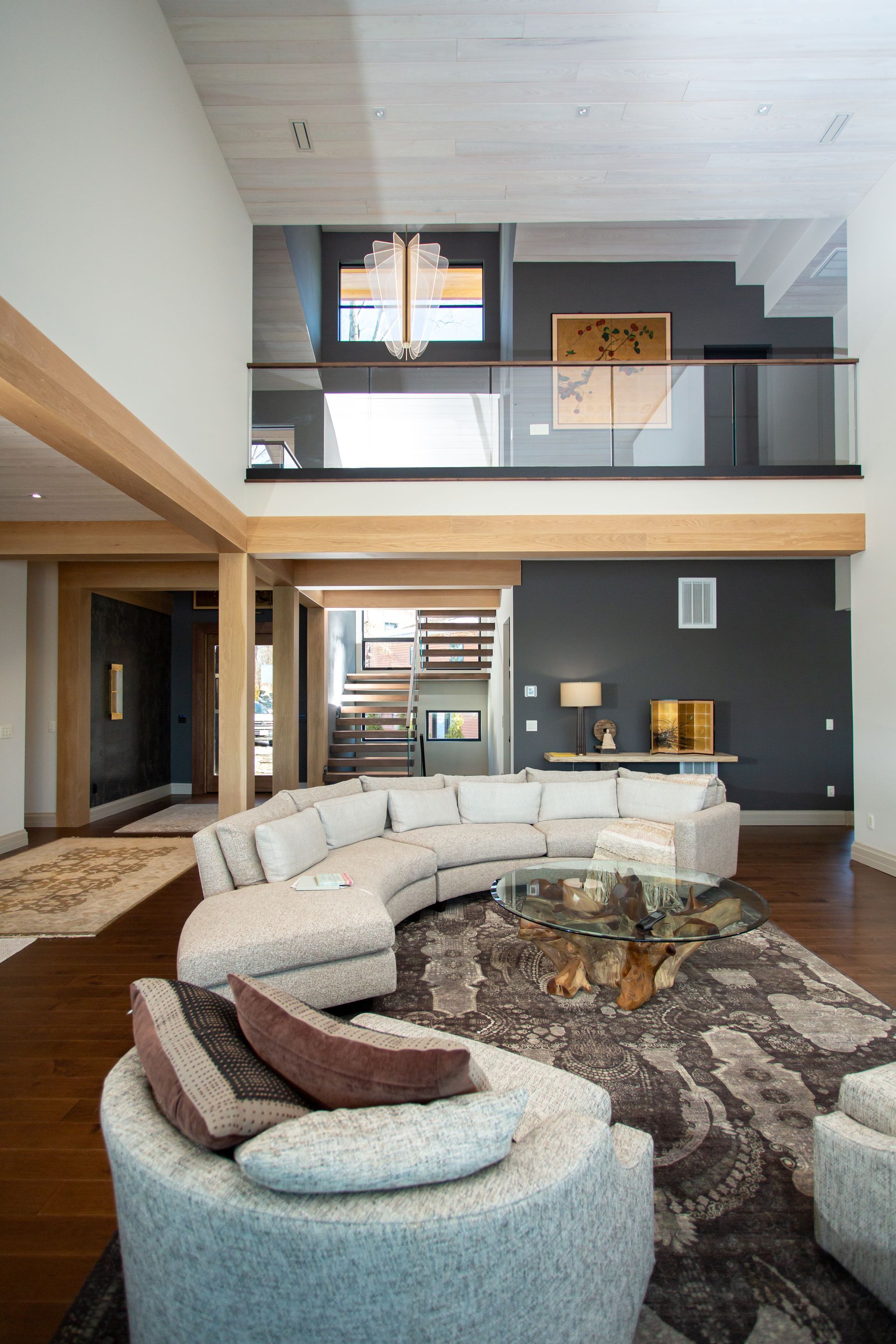 Spacious living room with curved sofa, dark accent wall, staircase, and open balcony.