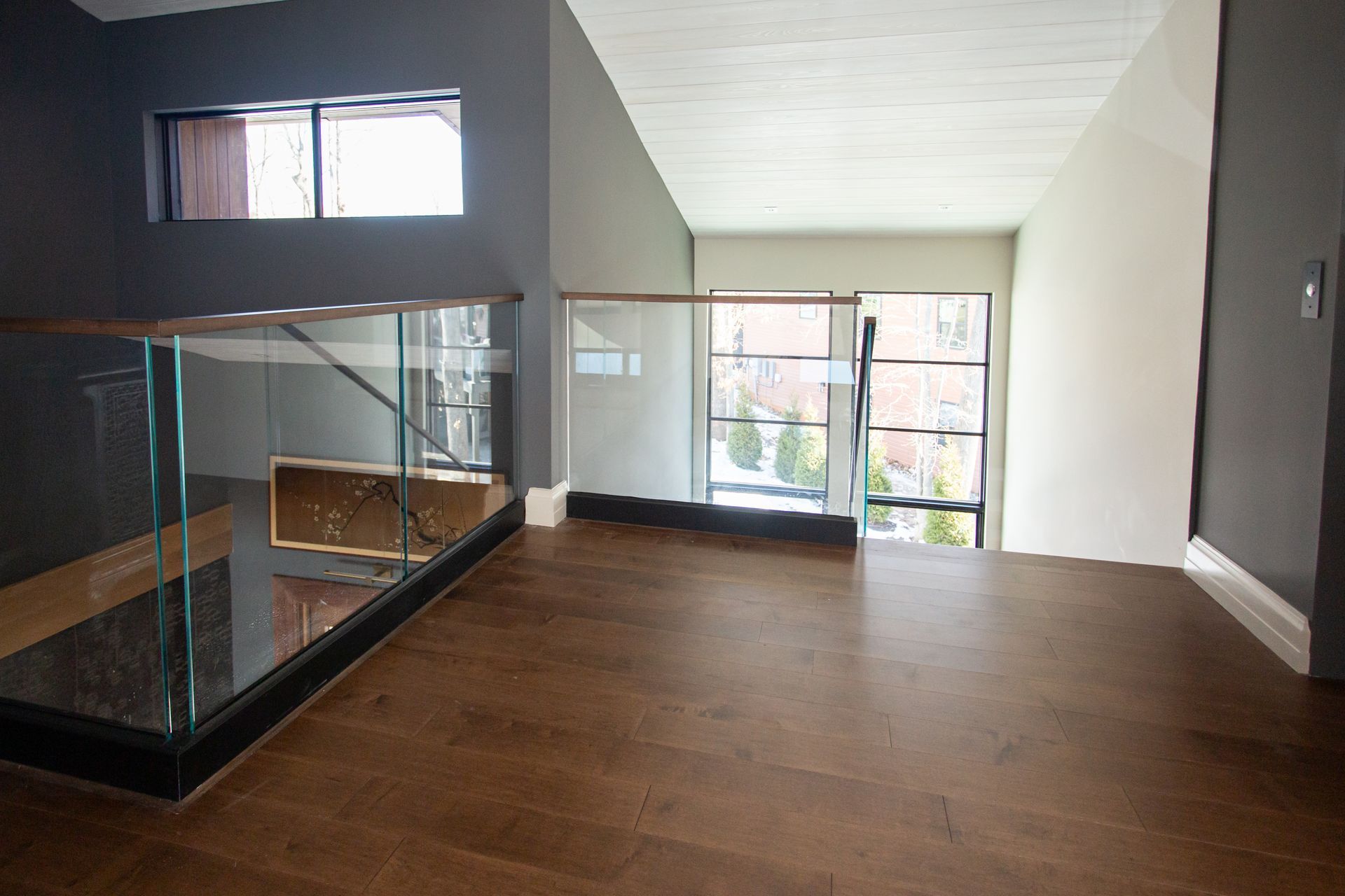 Interior view of a modern landing with wooden floor, glass railing, and large windows.