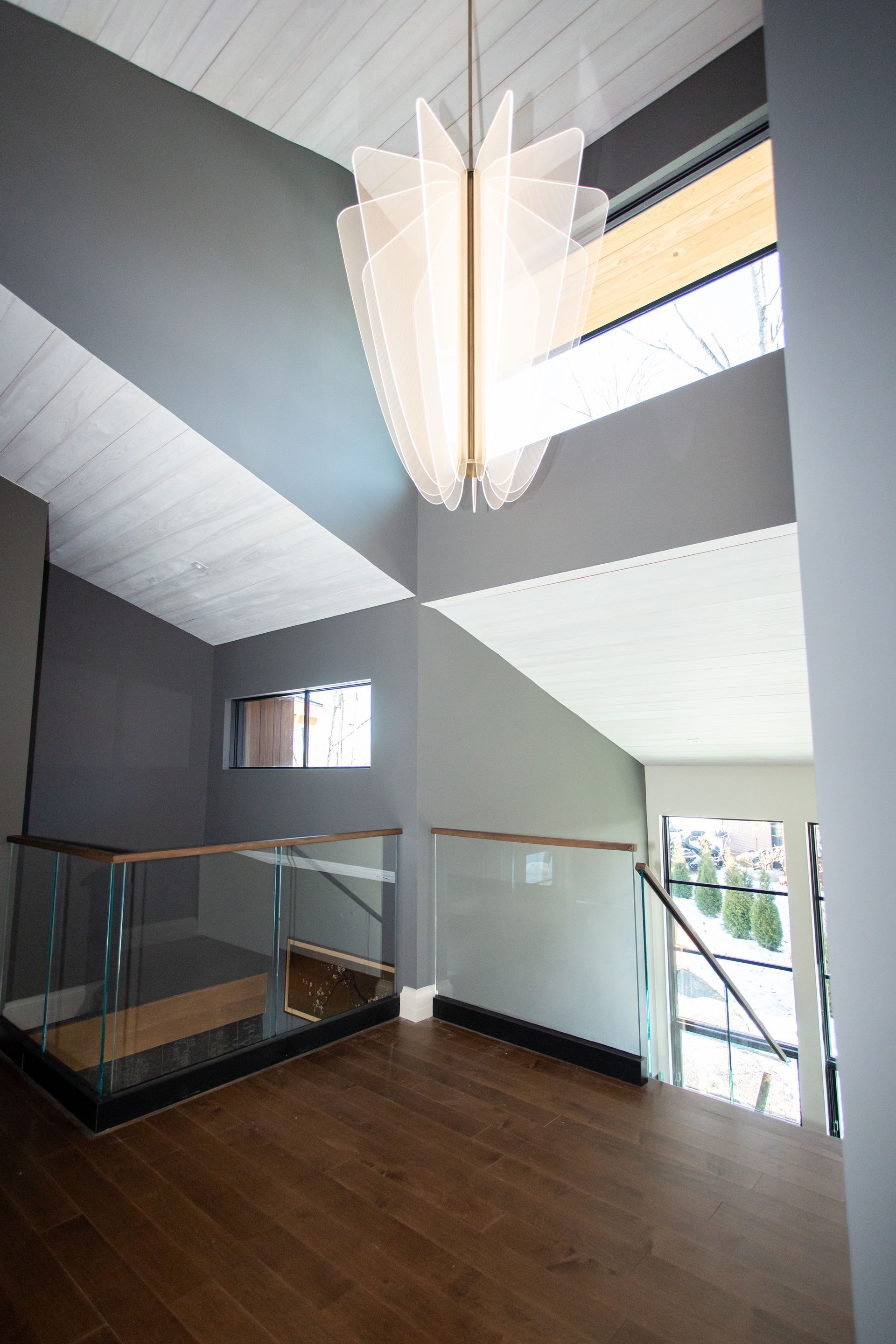 Interior view of a modern home hallway with wood floors, glass railings, and a geometric light fixture.