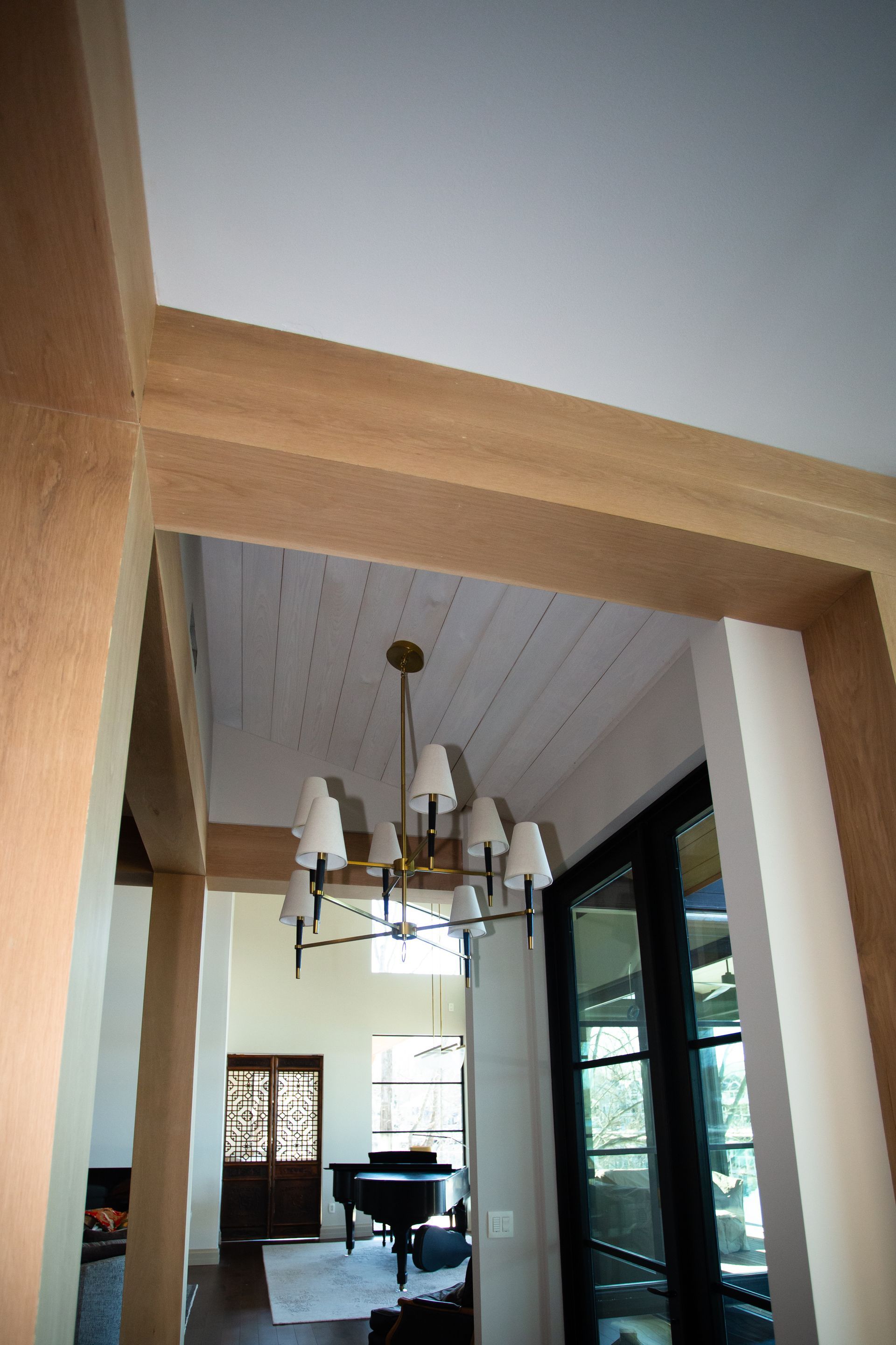 Hallway with white ceiling, chandelier, dark door, grand piano. Beige walls, light wood trim.