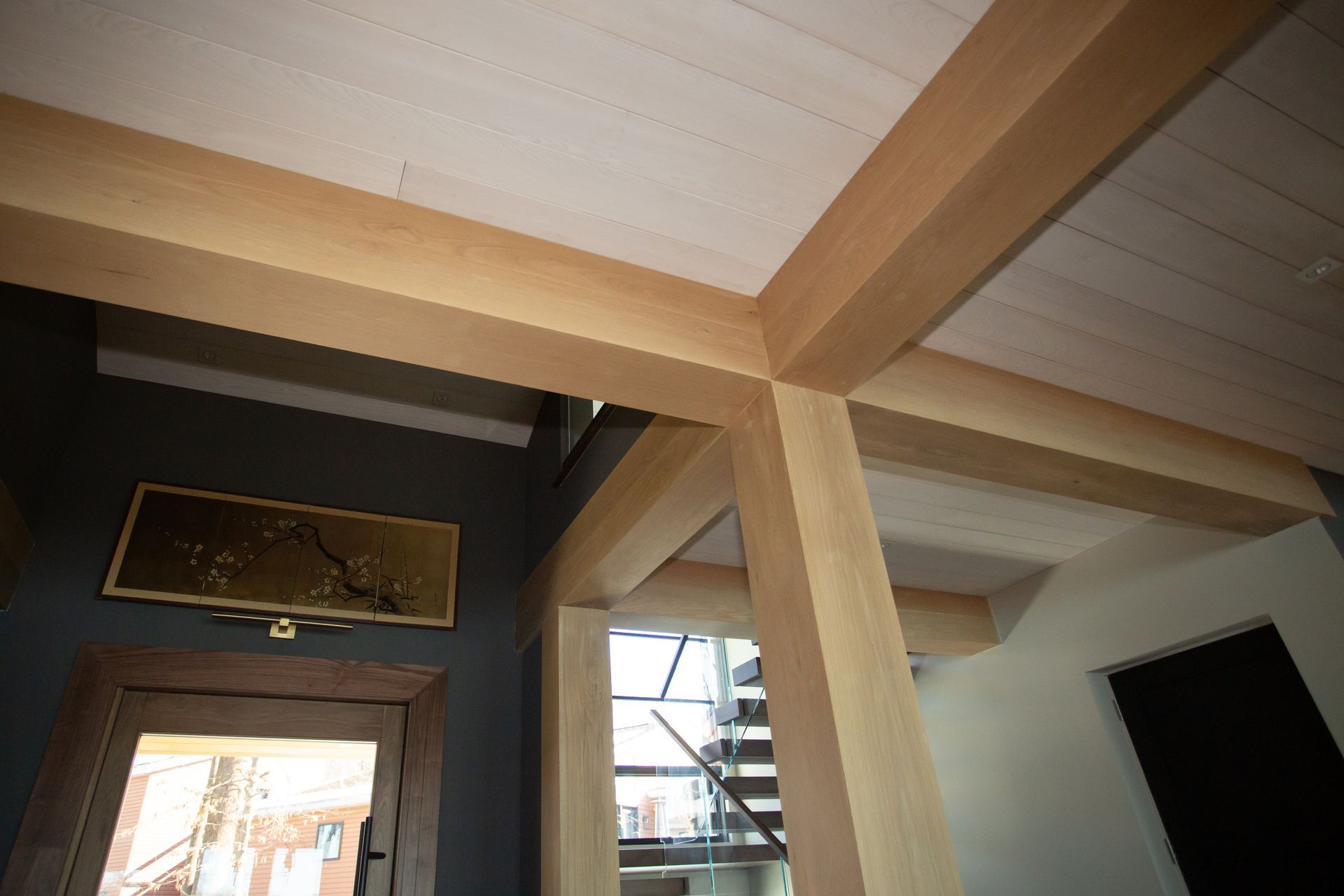 Wooden beams and ceiling of a modern home, with a view of a staircase through a doorway.