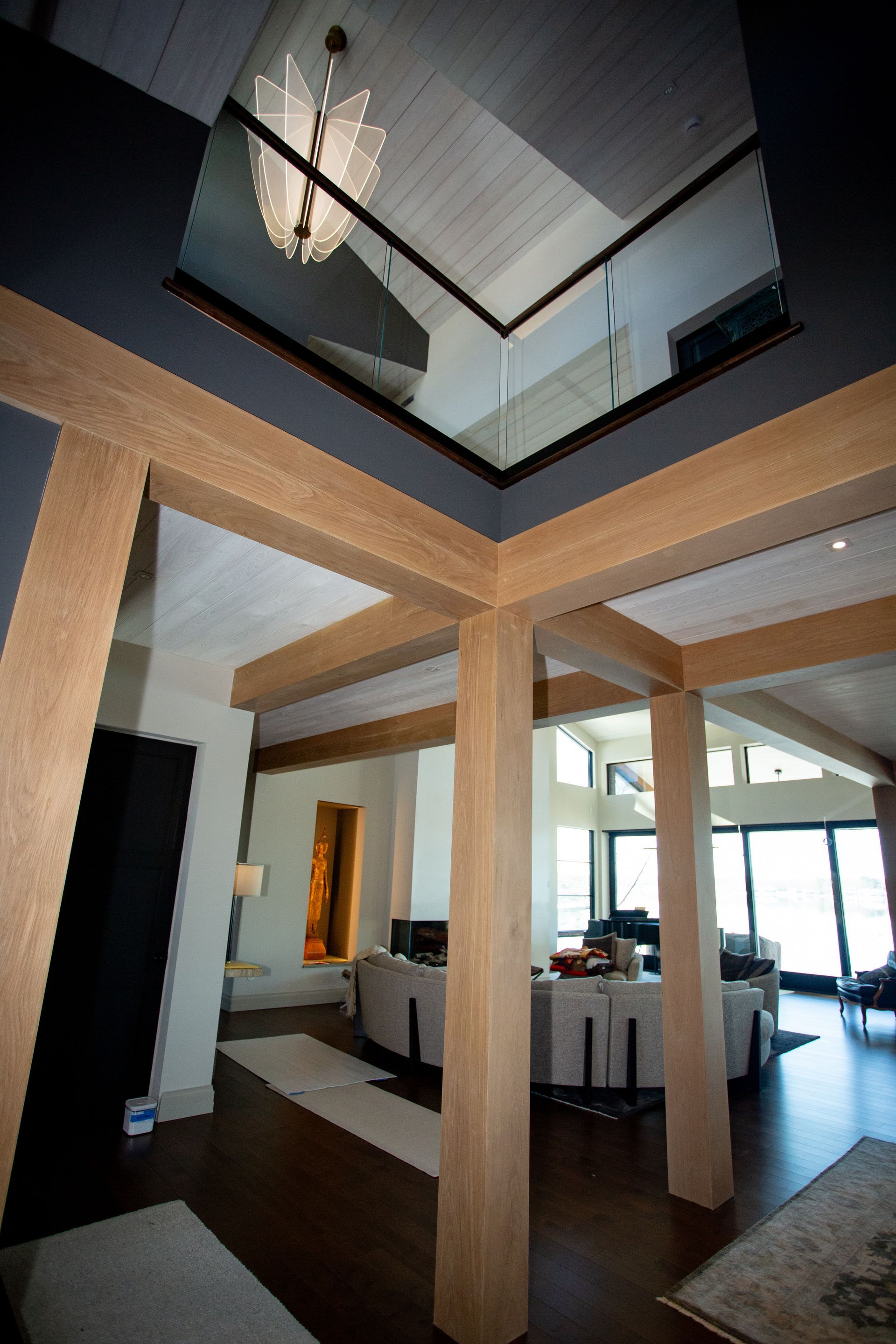 Interior with wooden beams, dark gray walls, and glass balcony. Light streams in.