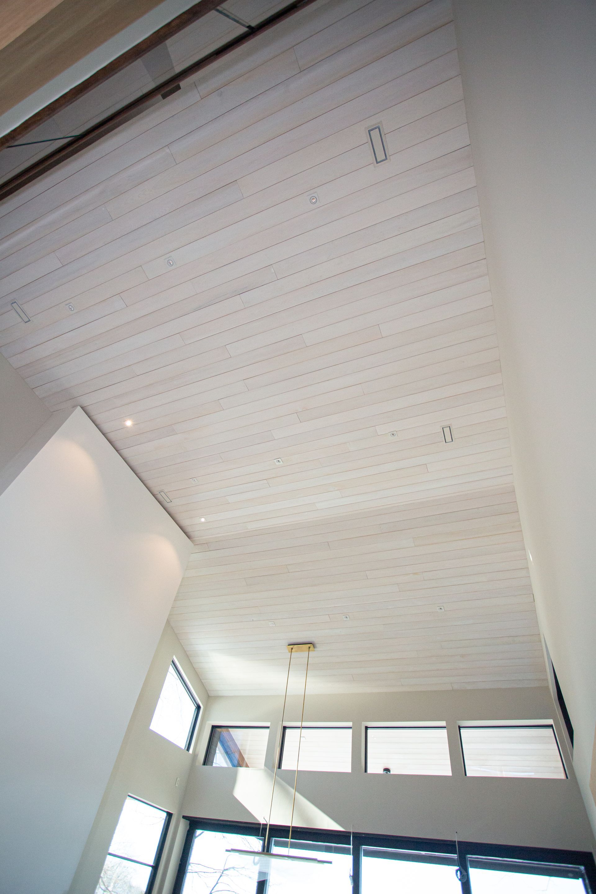 White-painted wood ceiling with recessed lighting. A modern room with tall windows and a pendant light fixture.