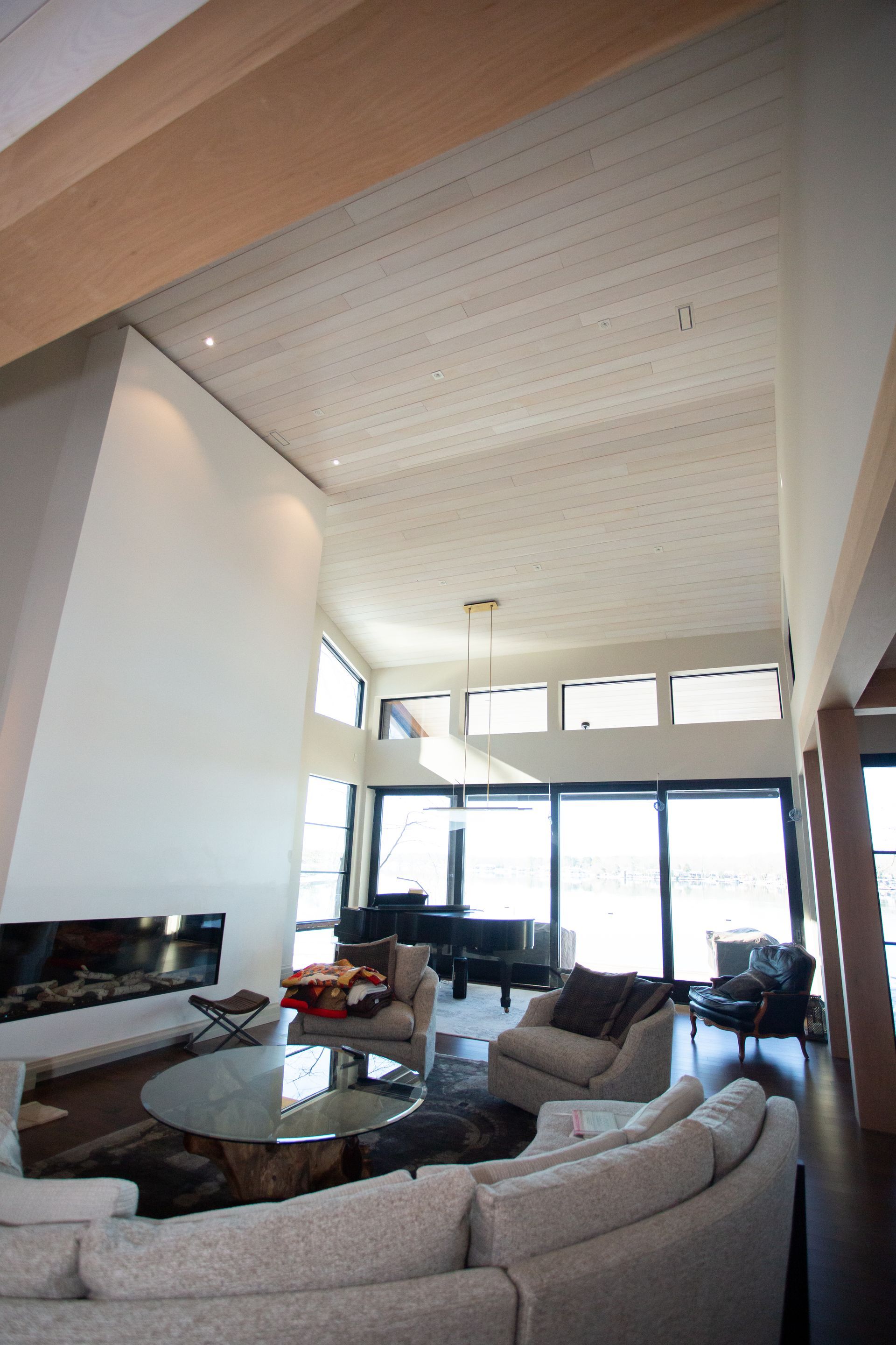 Spacious living room with high ceilings, fireplace, and piano, overlooking large windows.