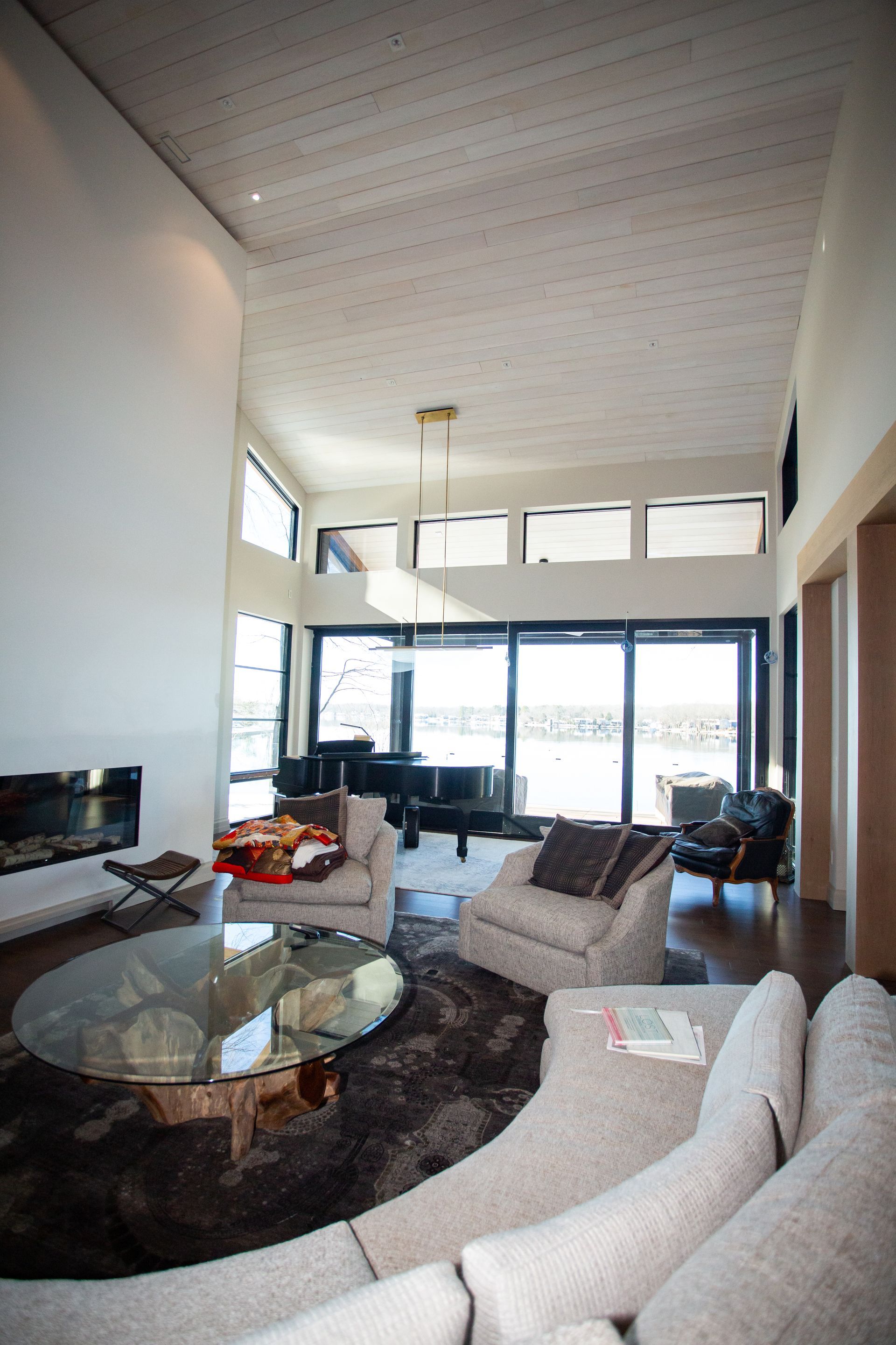 Spacious living room with high ceilings, glass doors overlooking a body of water, and a piano.