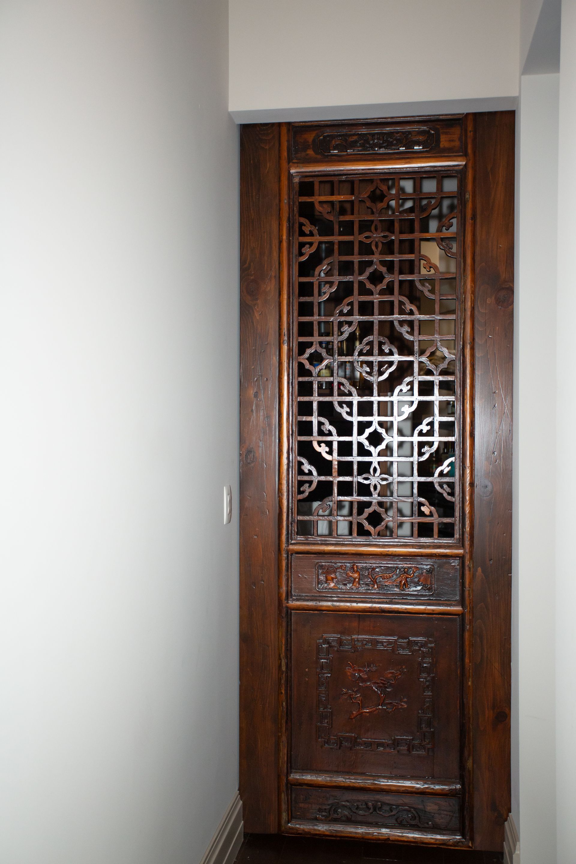 Wooden, ornate door with lattice design in a narrow hallway.