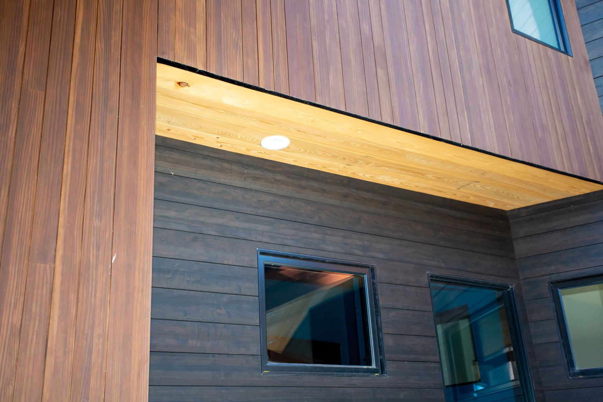 Wooden building exterior with illuminated soffit, windows, and dark wood siding.