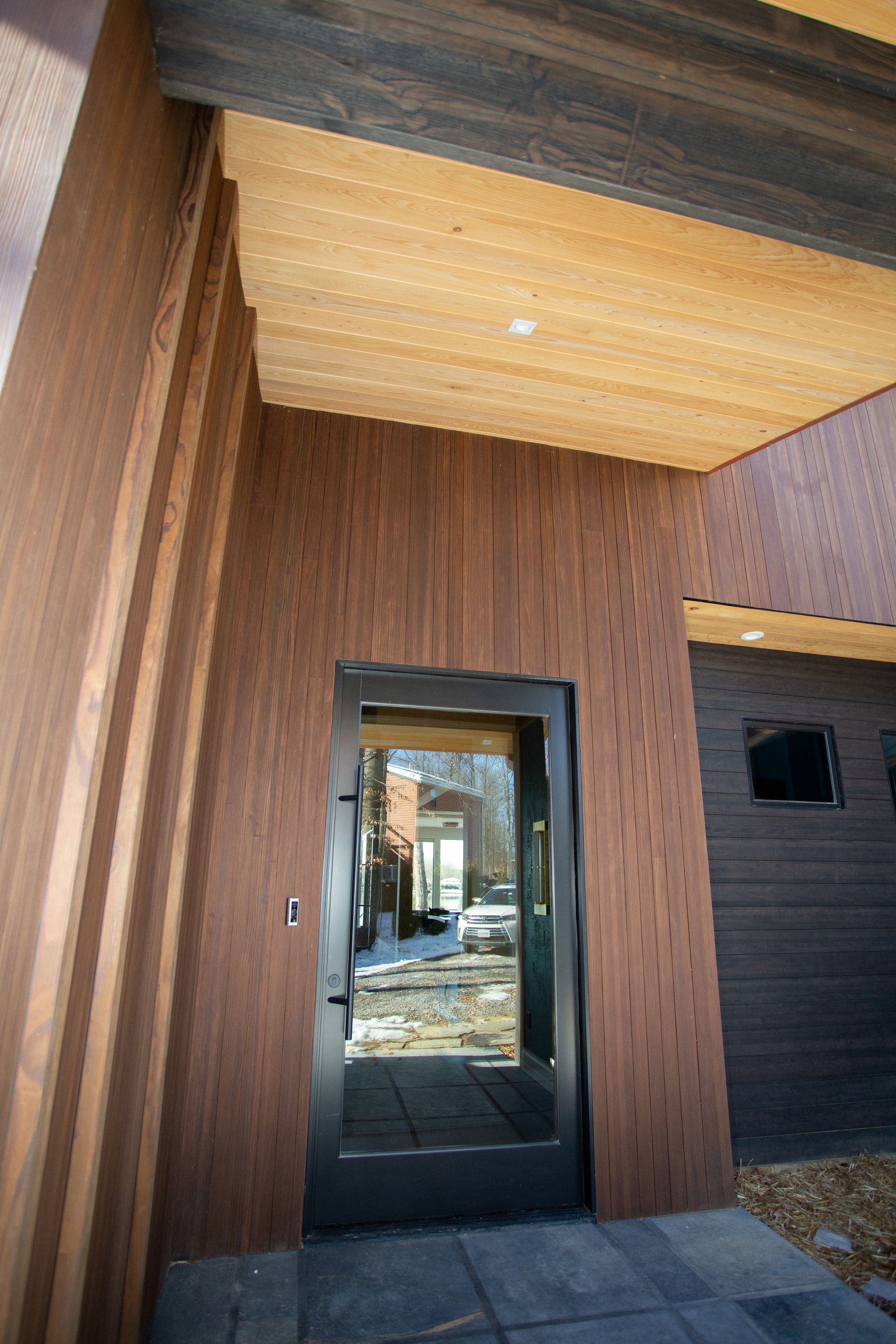 Entrance with a dark glass door and textured brown wood siding and ceiling.