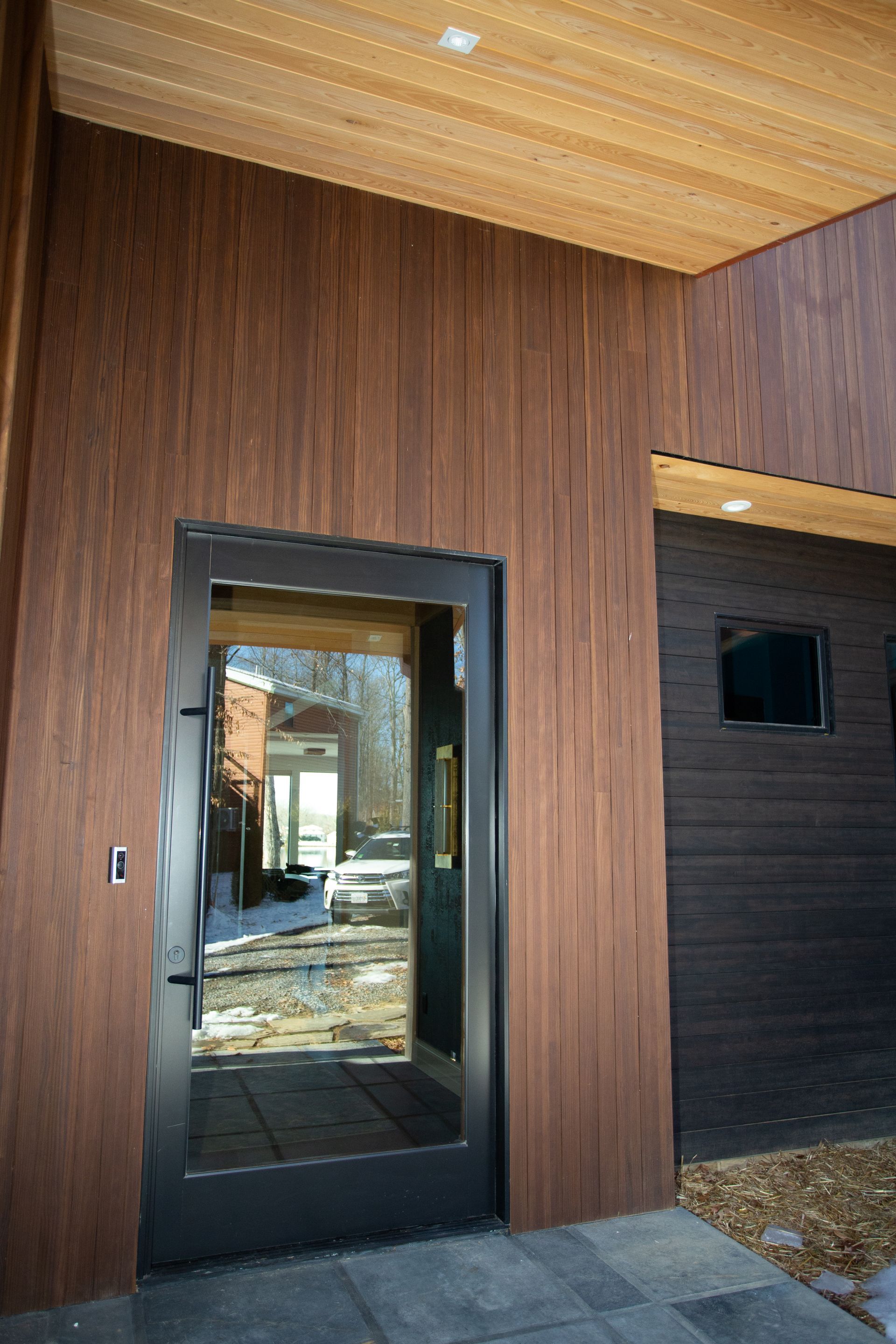 Exterior view: brown wood siding, glass door, dark trim, and stone patio.