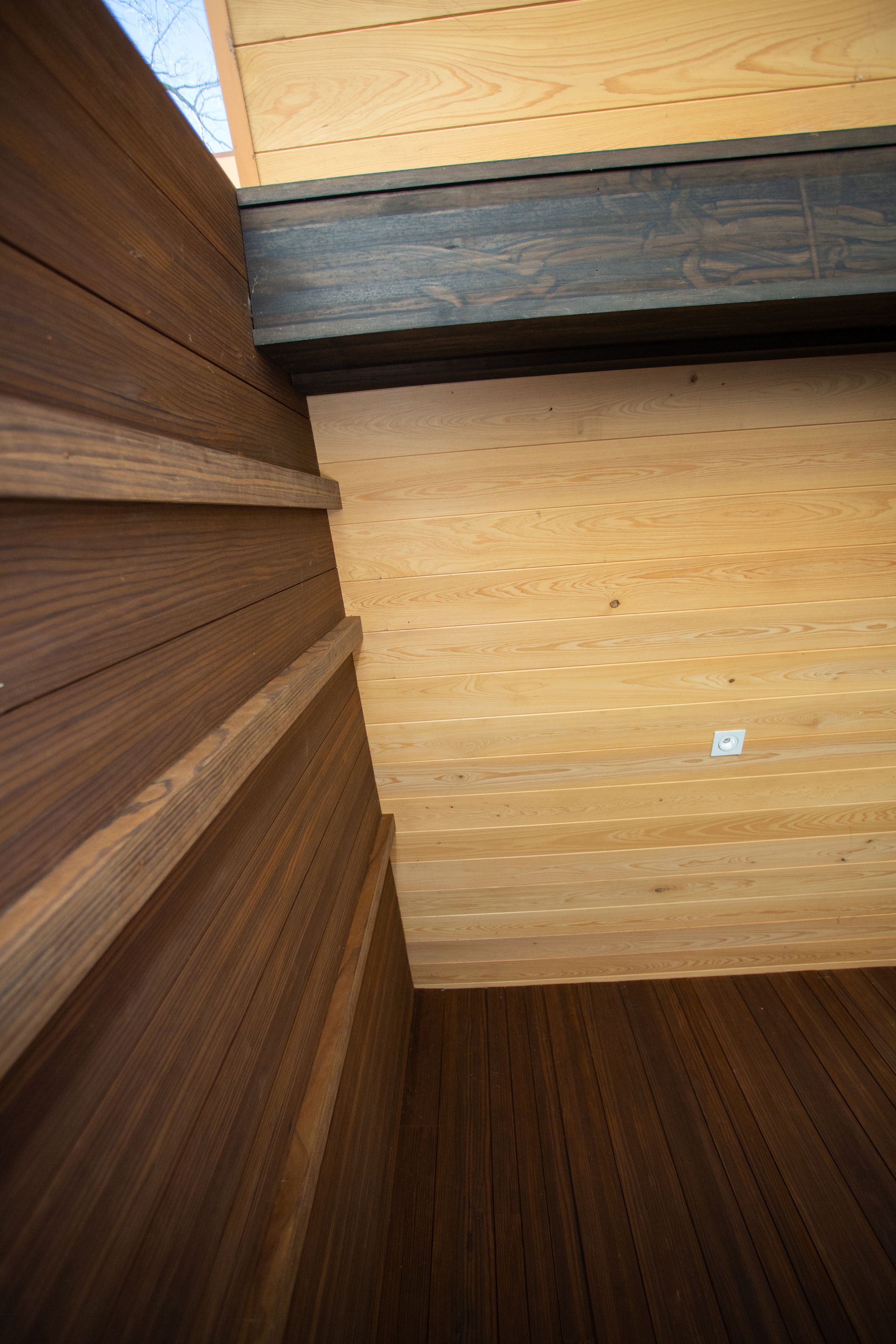 Wooden planks stacked, brown and tan, in a corner. Dark wooden beam above.