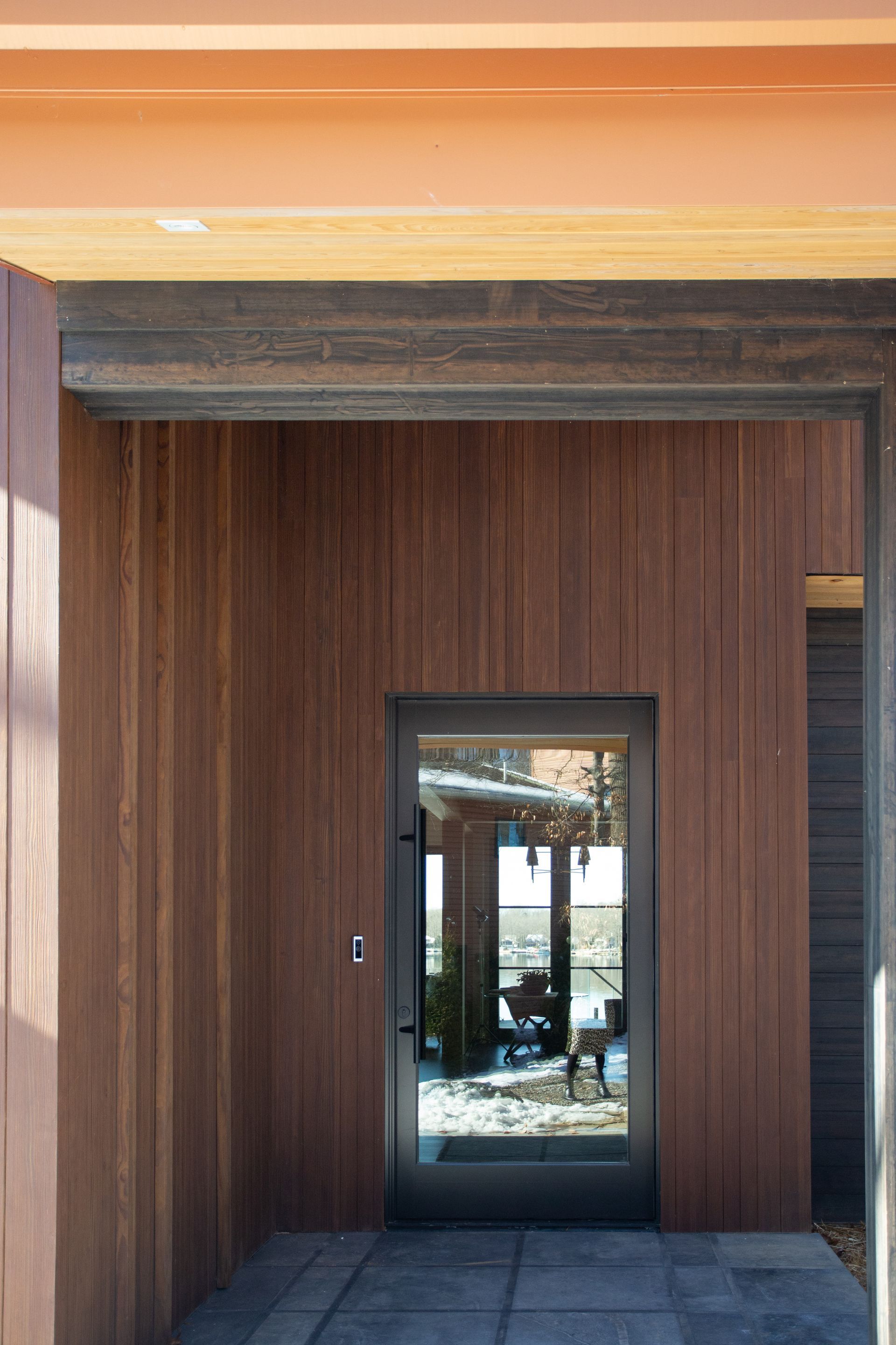 Exterior doorway framed by wood siding. Dark glass door reflects interior.