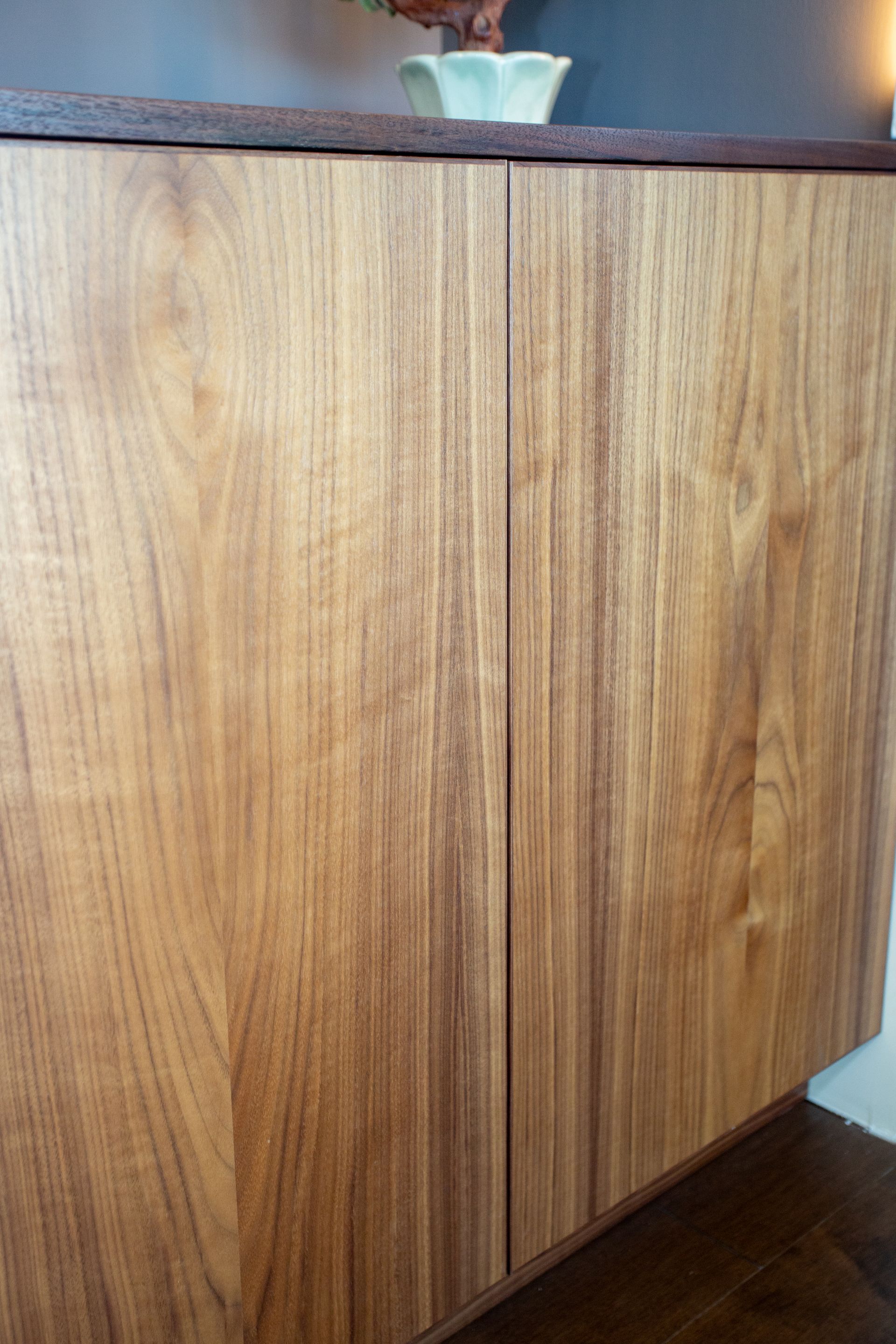 Wooden cabinet with two doors, brown wood grain, top with a dark stained edge, light green bowl on top.