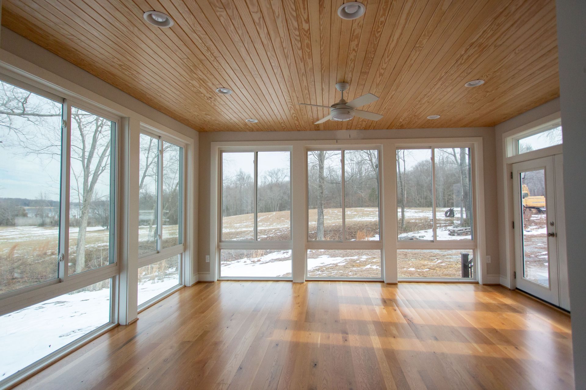 Sunroom with large windows, wood ceiling, and hardwood floors overlooking a snowy landscape.