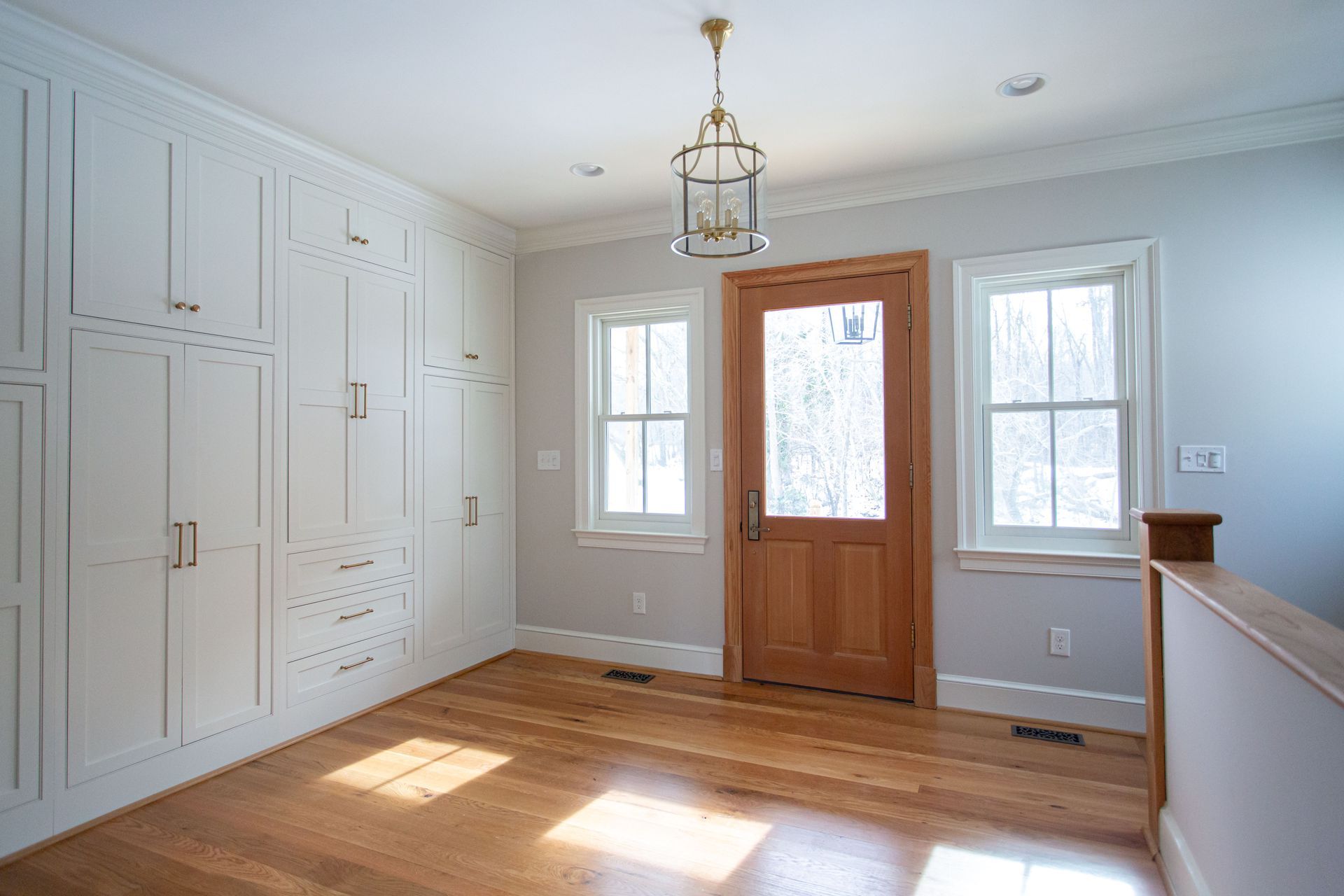 Room with wood floor, white built-in cabinets, a wooden door with window, and a hanging light fixture.