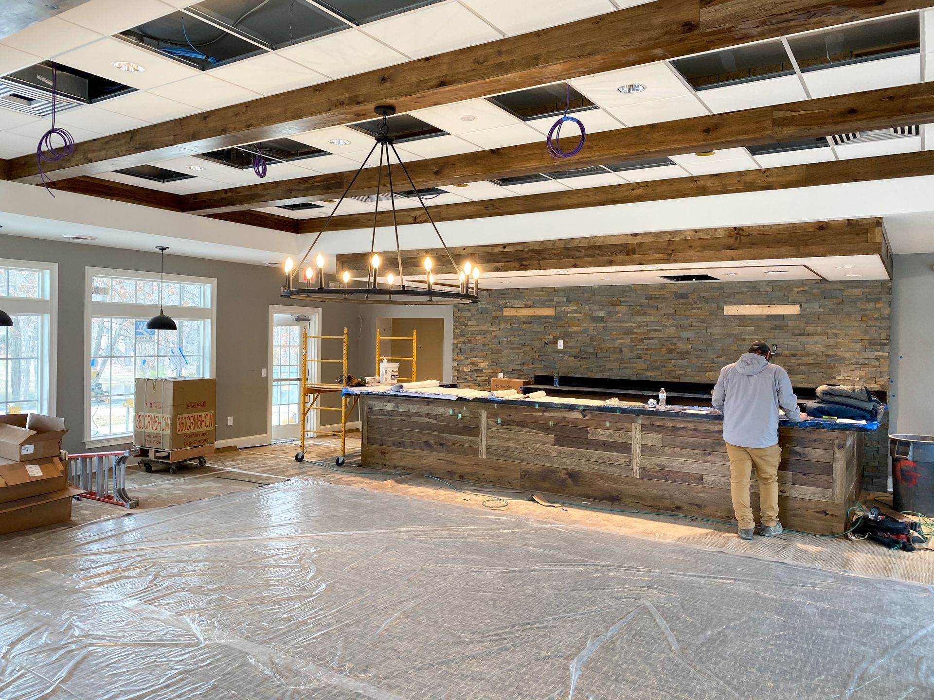 Interior construction: Man working at a bar with wood and stone features. Exposed ceiling beams and windows.