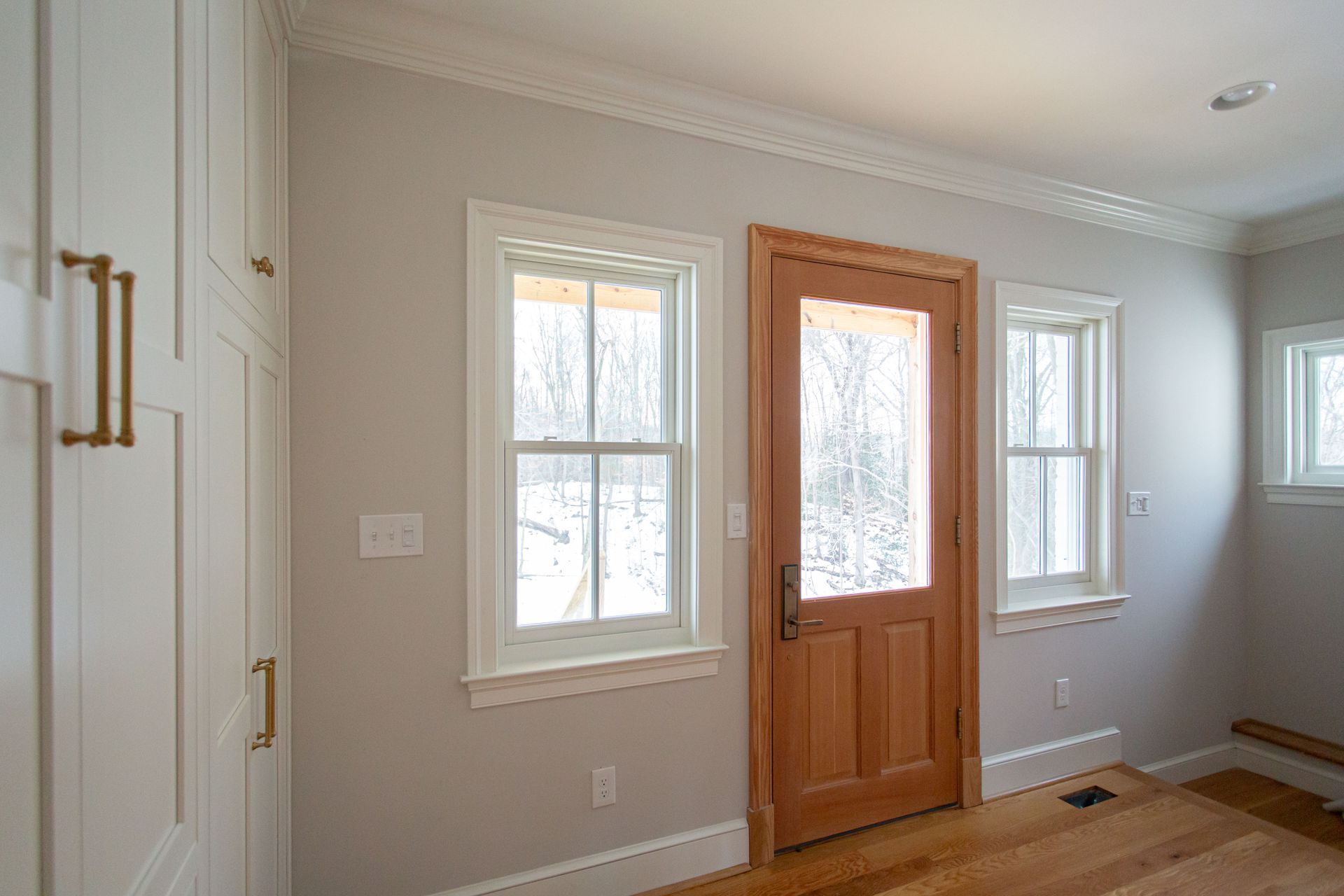 White-walled room with wooden door, windows, and built-in white cabinets with gold handles.