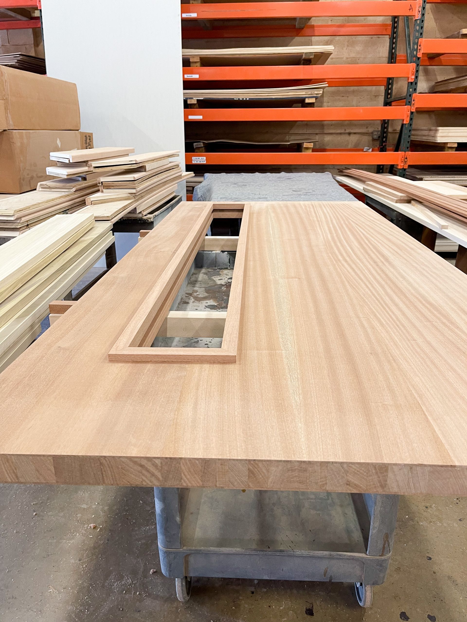 Large wooden table with rectangular cutout, in a workshop setting with wood shelving.