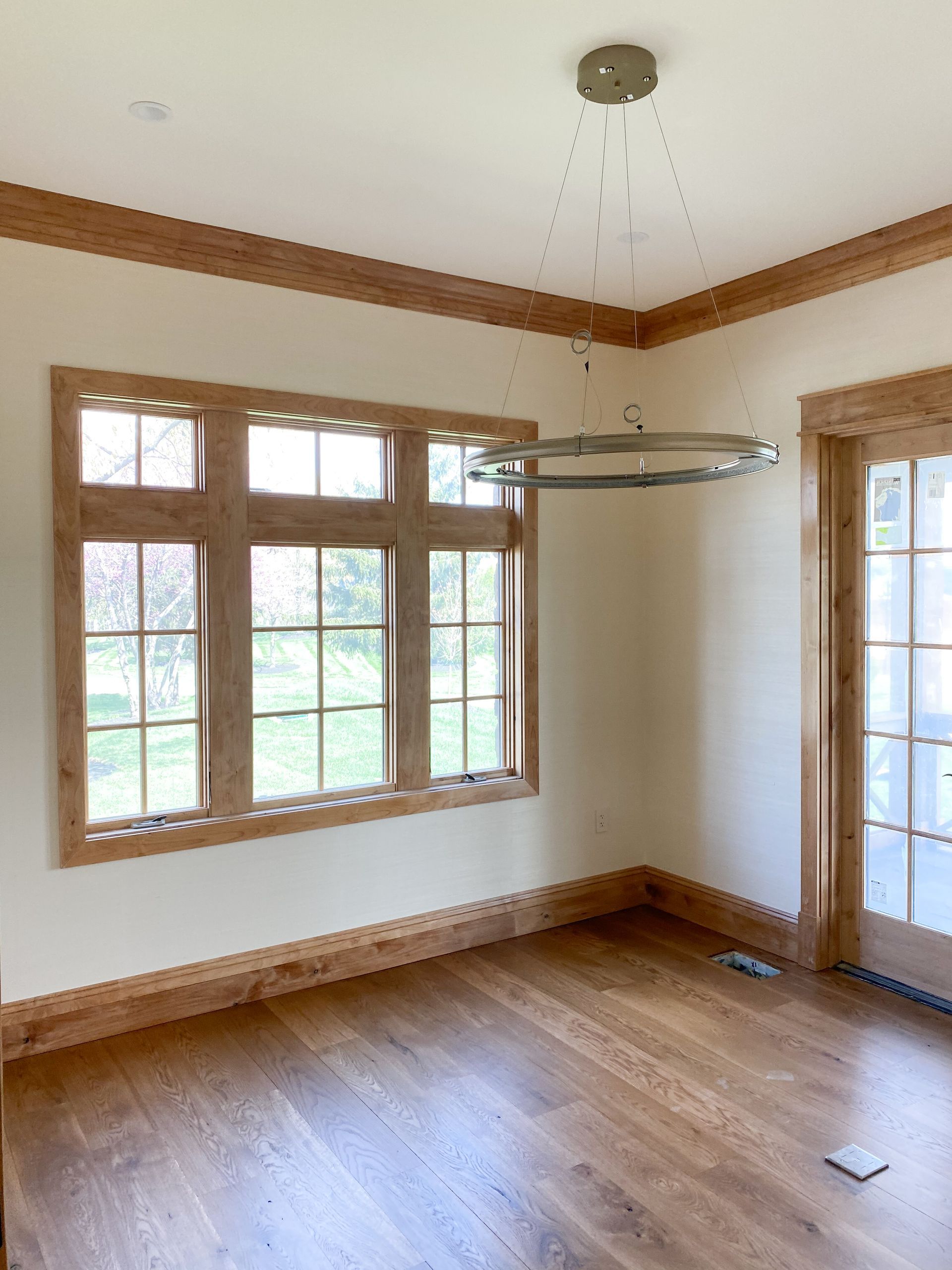 Empty room with wood floors, trim, and window frames; a large window, a door, and a decorative light fixture.