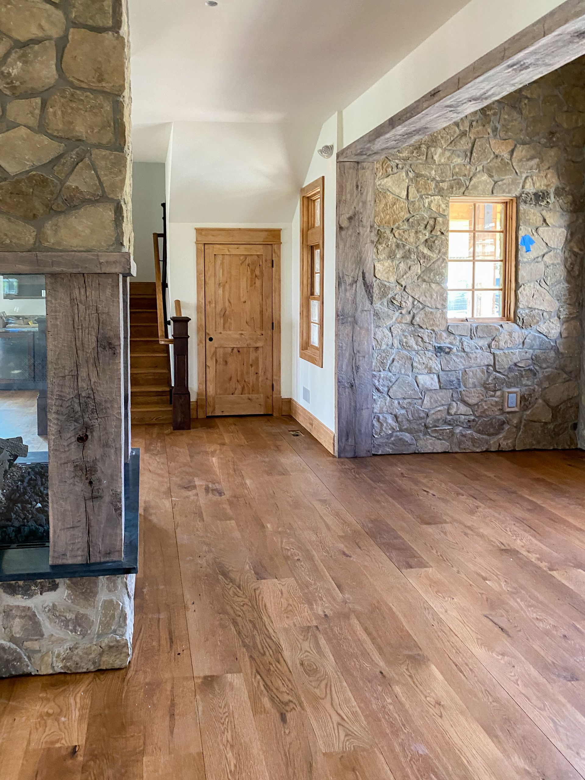 Stone-walled interior with wooden floors, door, window, and staircase. Fireplace with wooden beam mantle on the left.