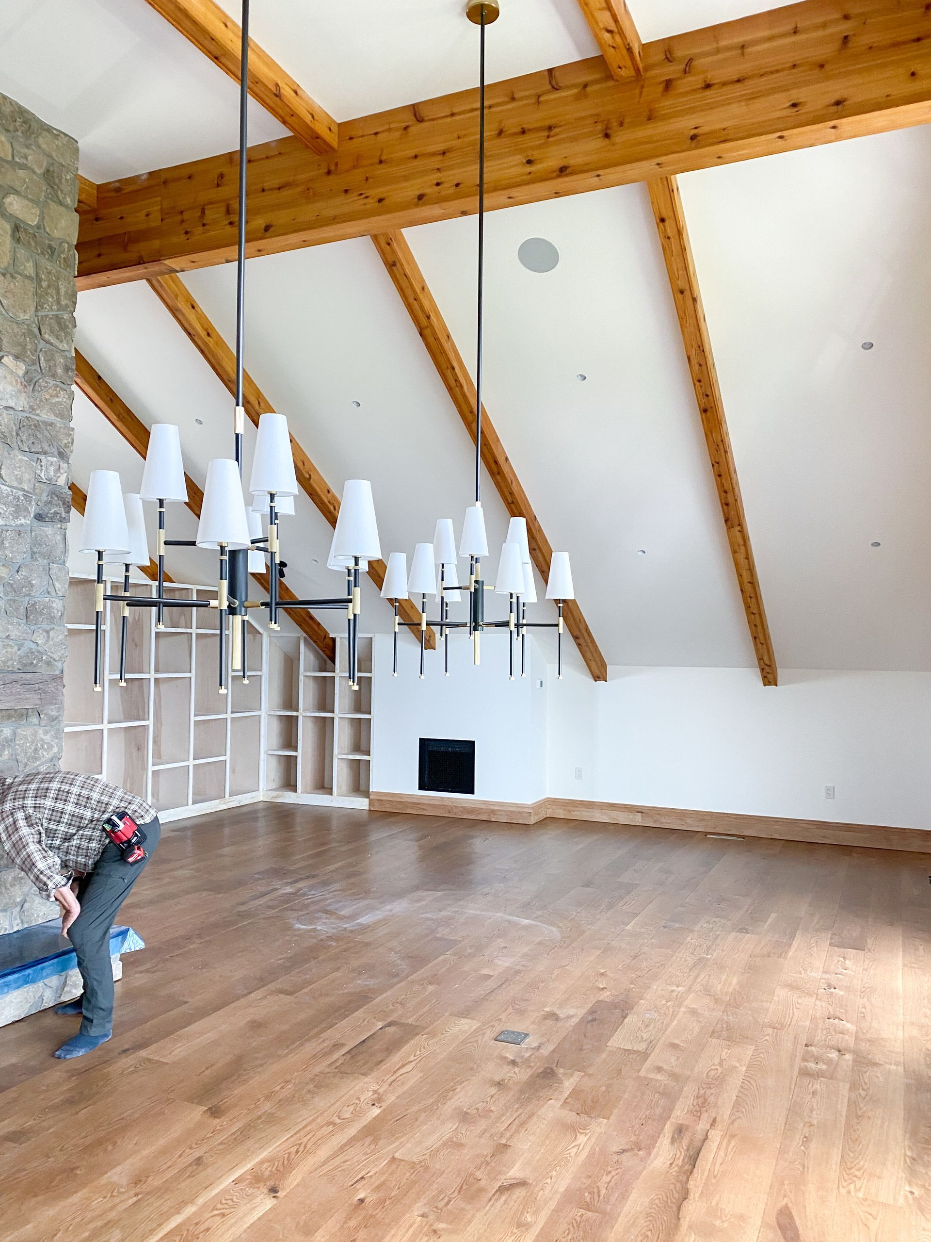 Interior of a spacious room with hardwood floors, a stone wall, and exposed wooden beams. A person works on the floor.