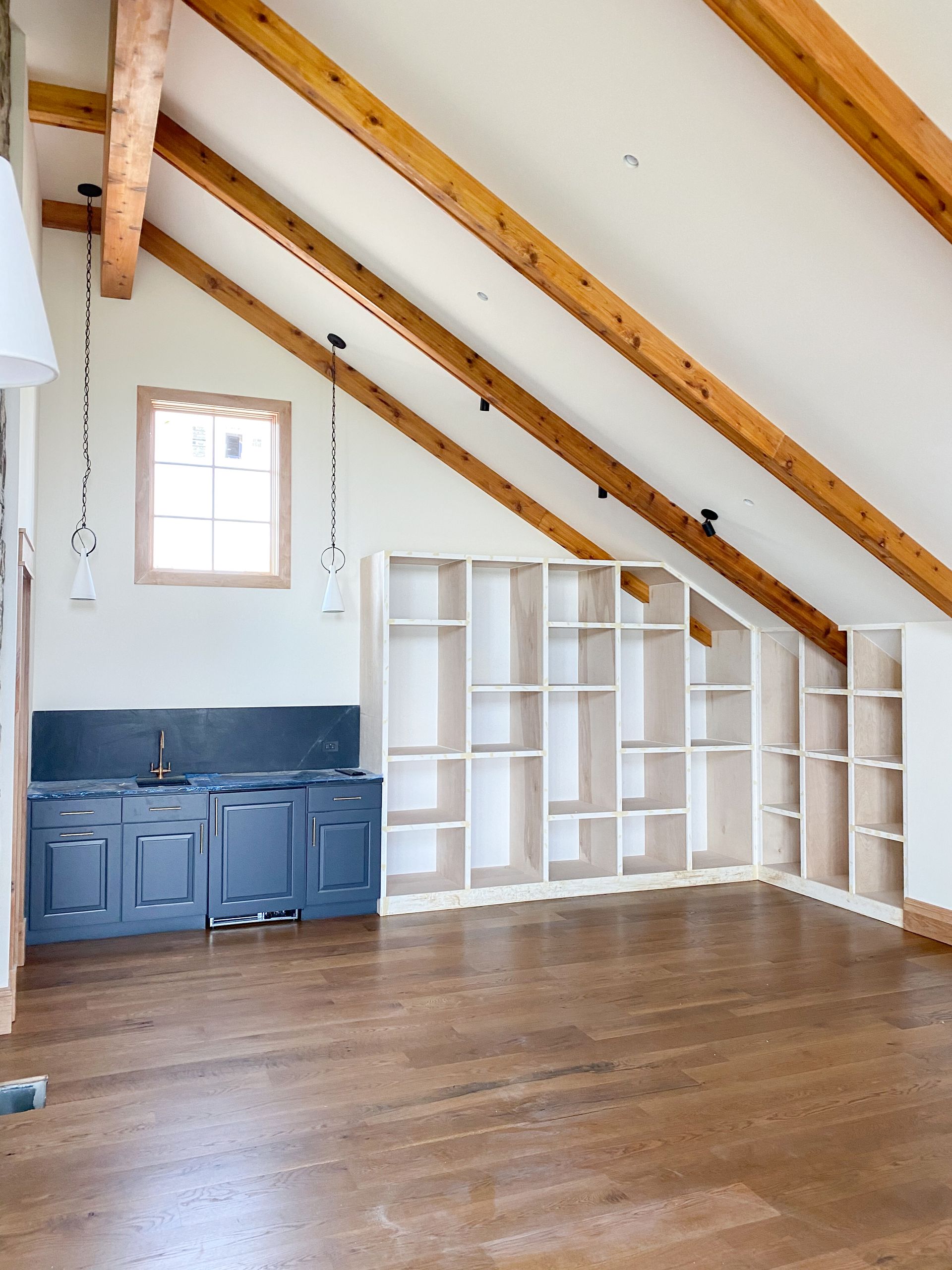 Room with wood beams, built-in shelves, blue cabinets, and a small window.