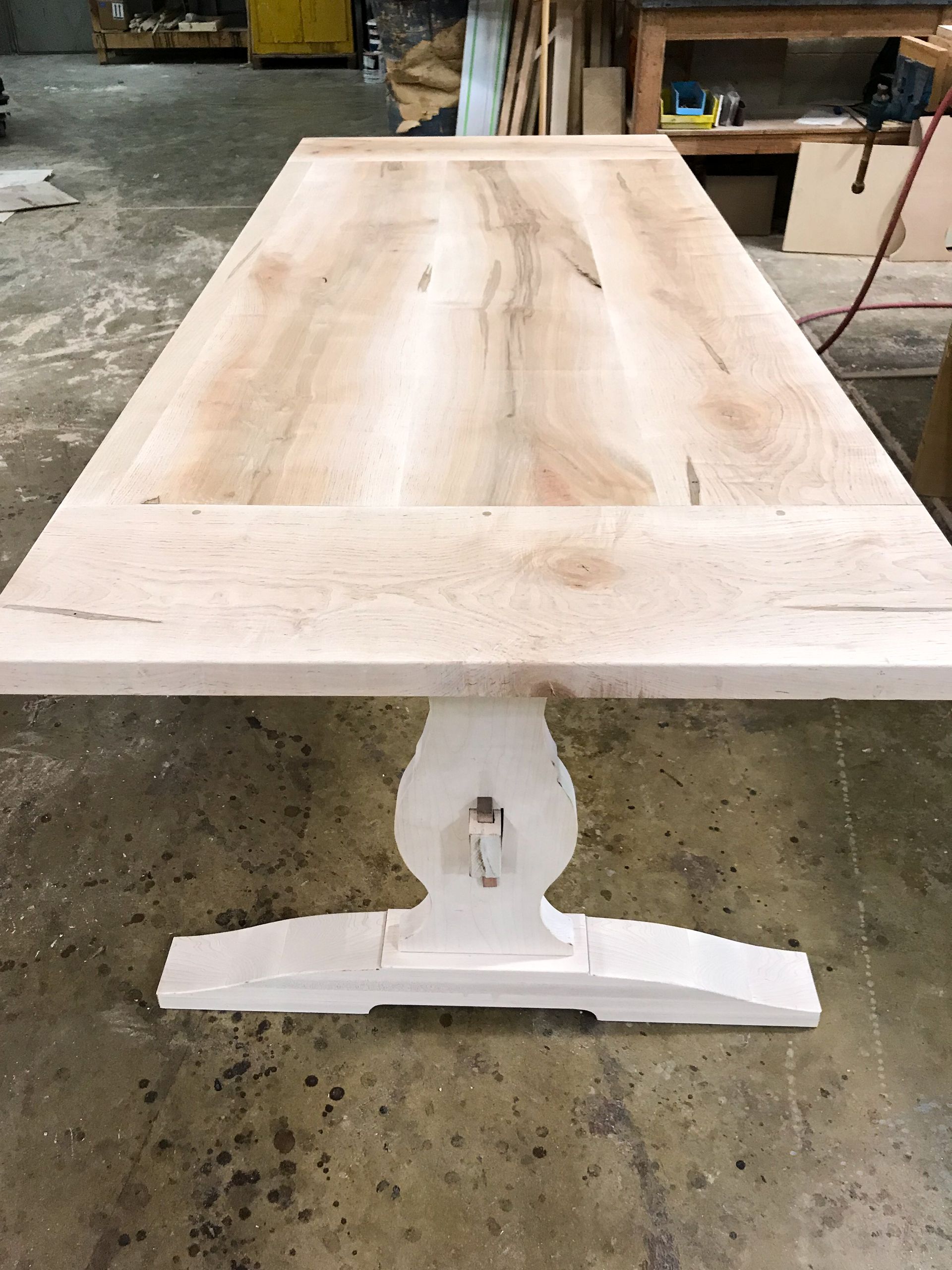 Light wood farmhouse-style dining table with white pedestal base, indoors.