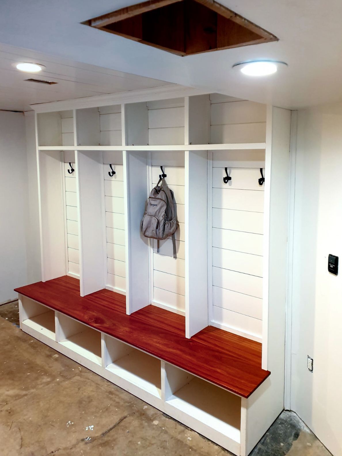 Built-in white lockers with red-stained benches, hooks, and open storage. One locker has a backpack hanging.