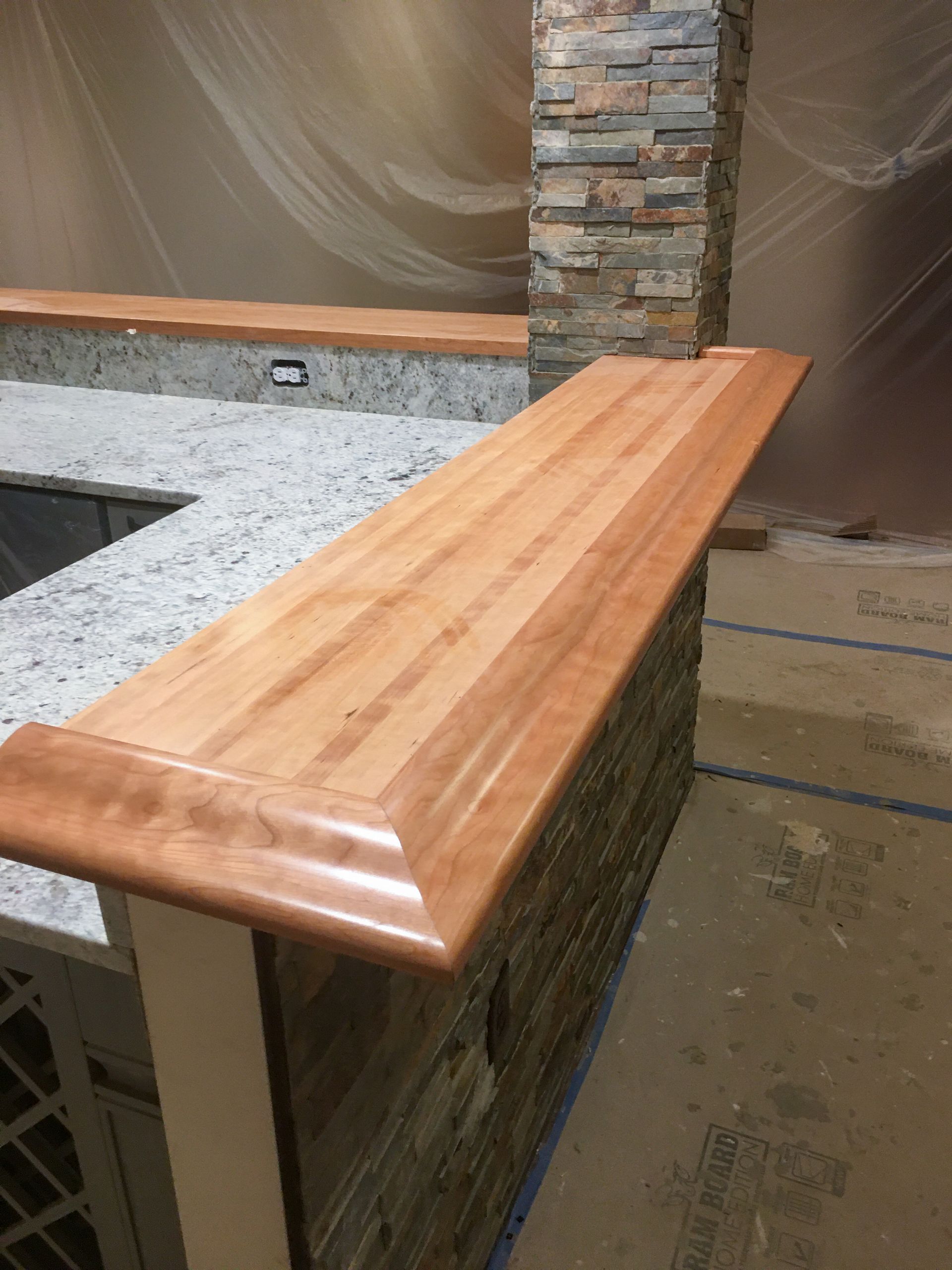 Wooden bar top with a beveled edge, atop a stone and white cabinet.