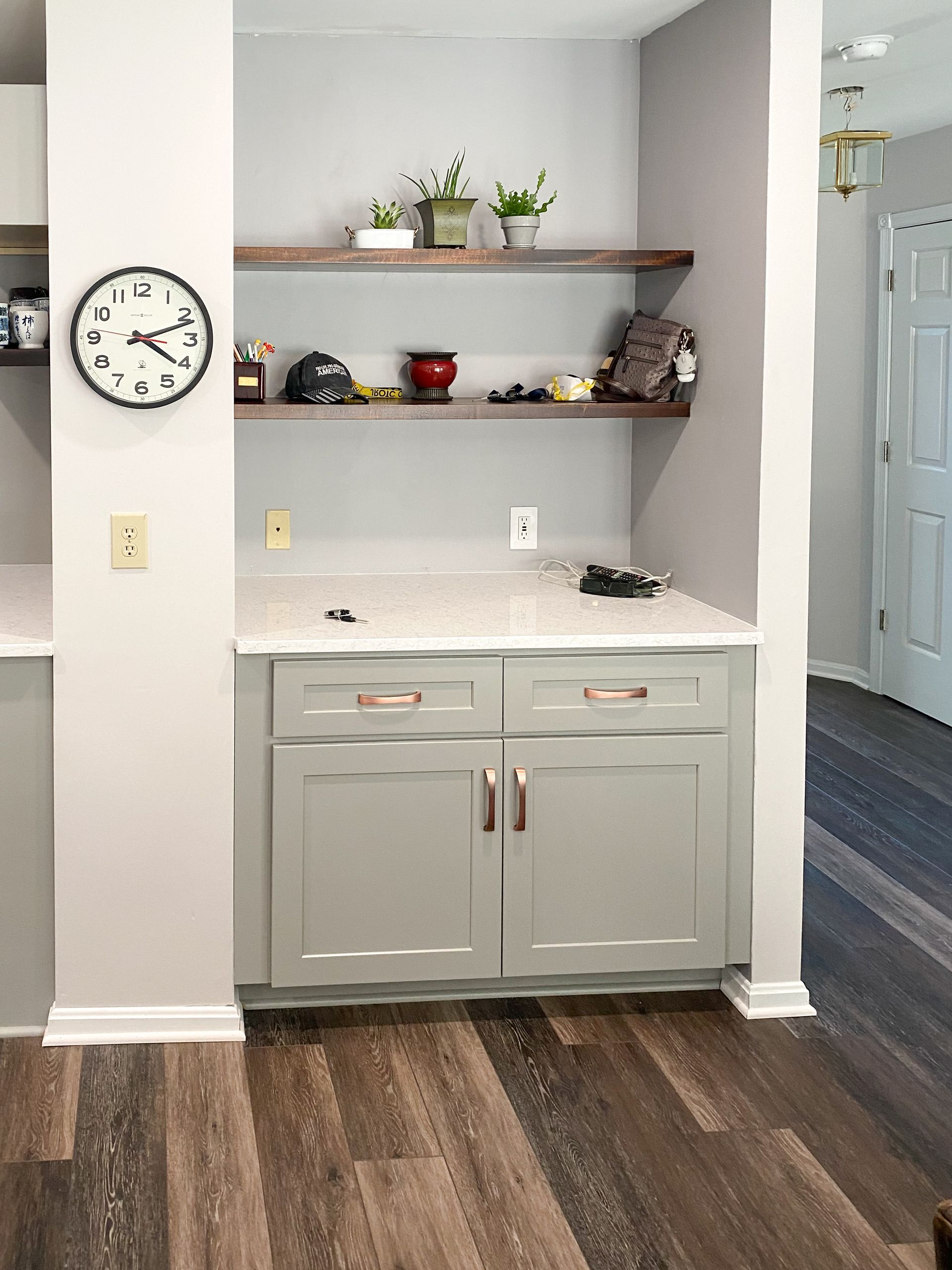 Gray built-in cabinet with floating shelves, copper hardware, and countertop. Dark wood flooring.