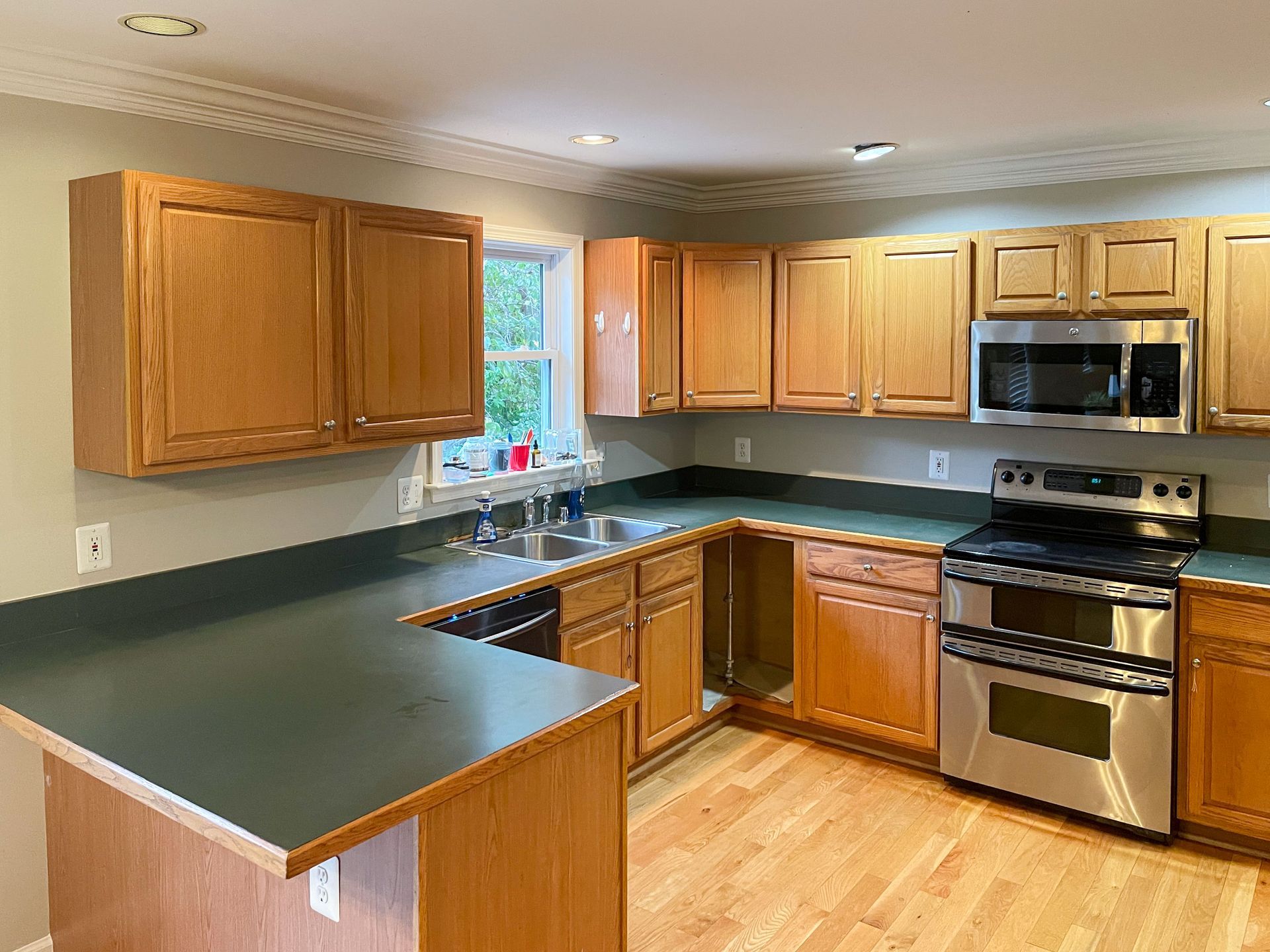 Oak kitchen cabinets with dark green countertops and stainless steel appliances.