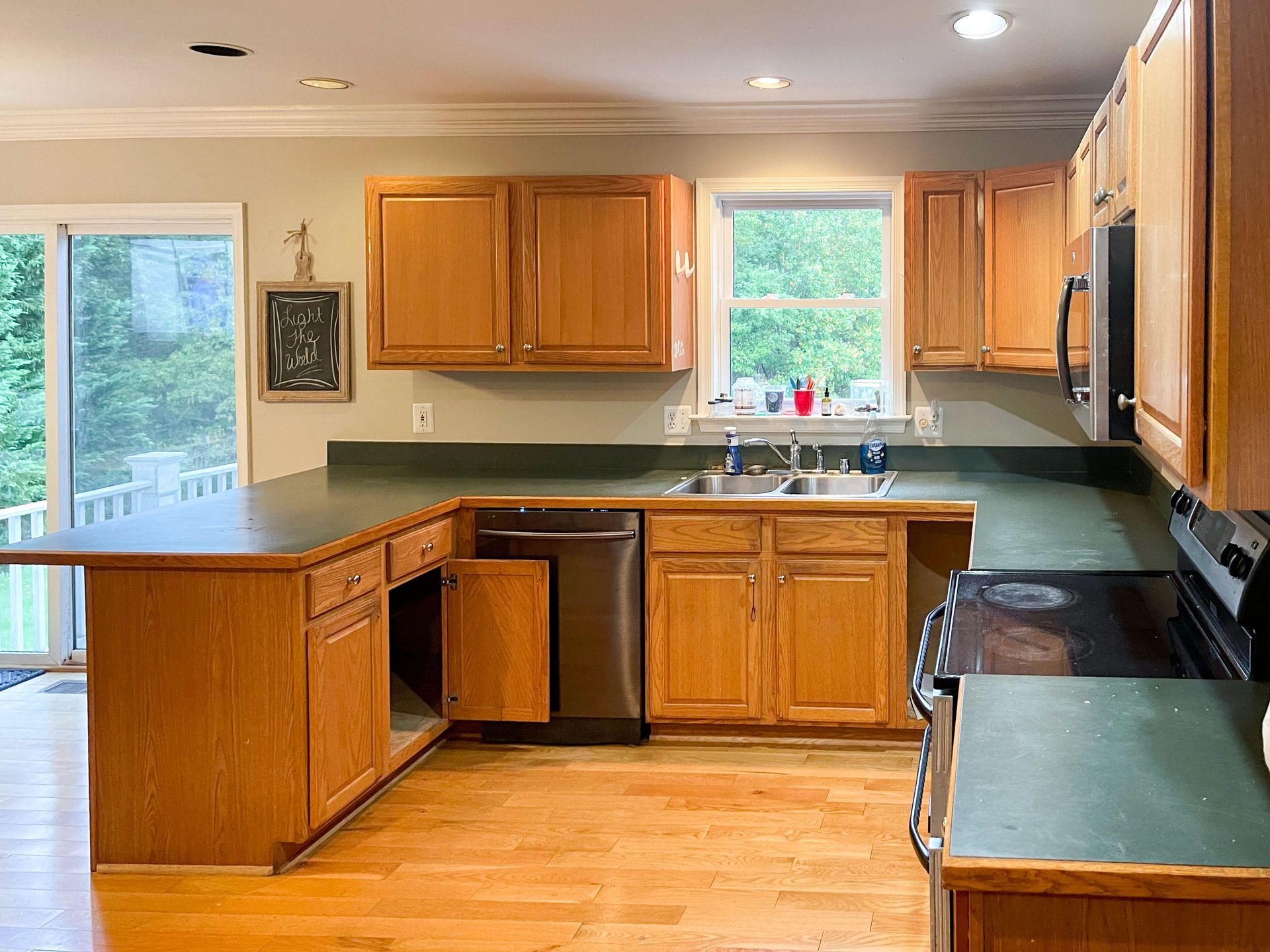 Kitchen with oak cabinets, dark green countertops, and a window overlooking greenery.