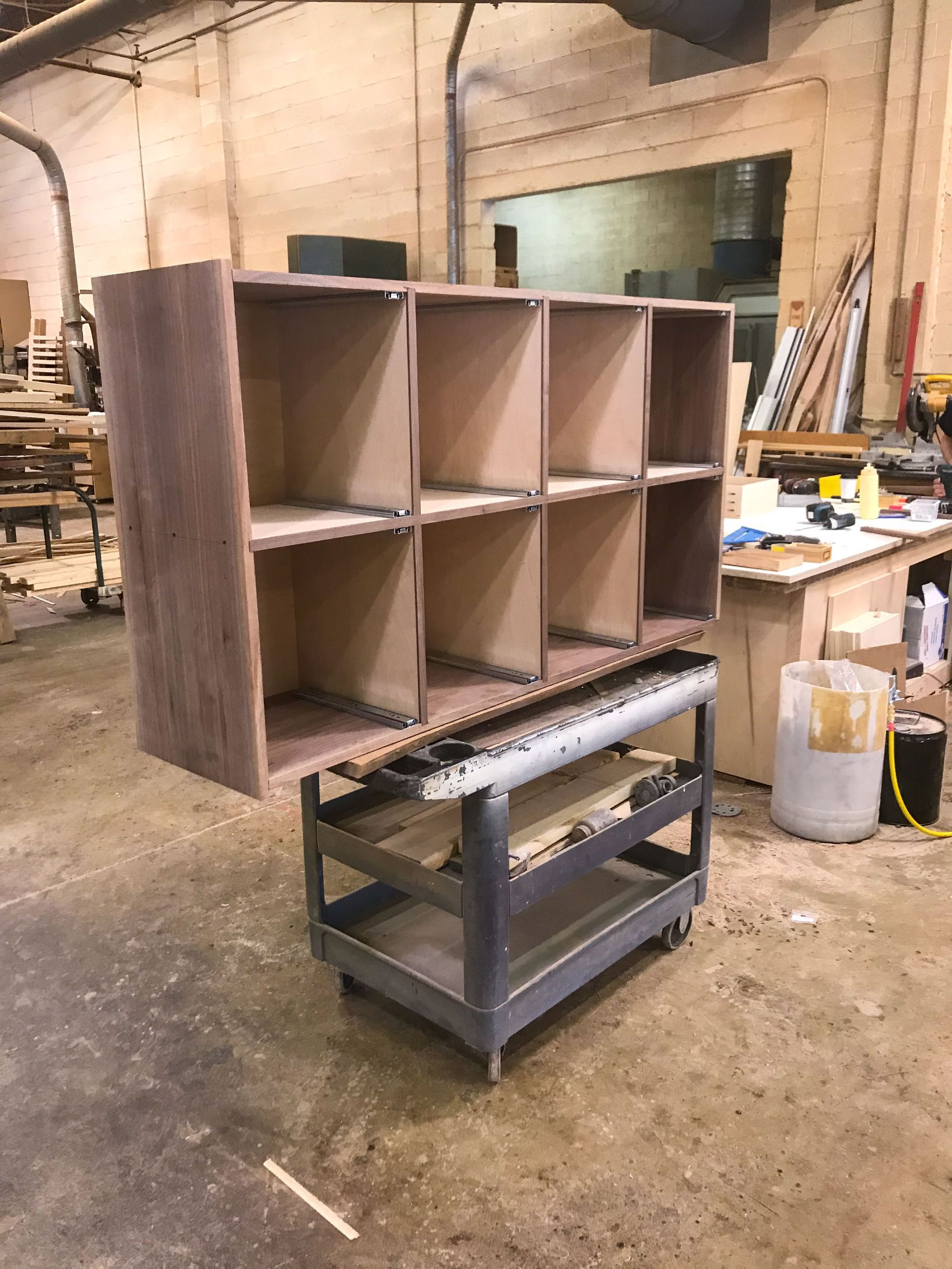 Wooden shelving unit being assembled on a wheeled cart in a workshop setting.