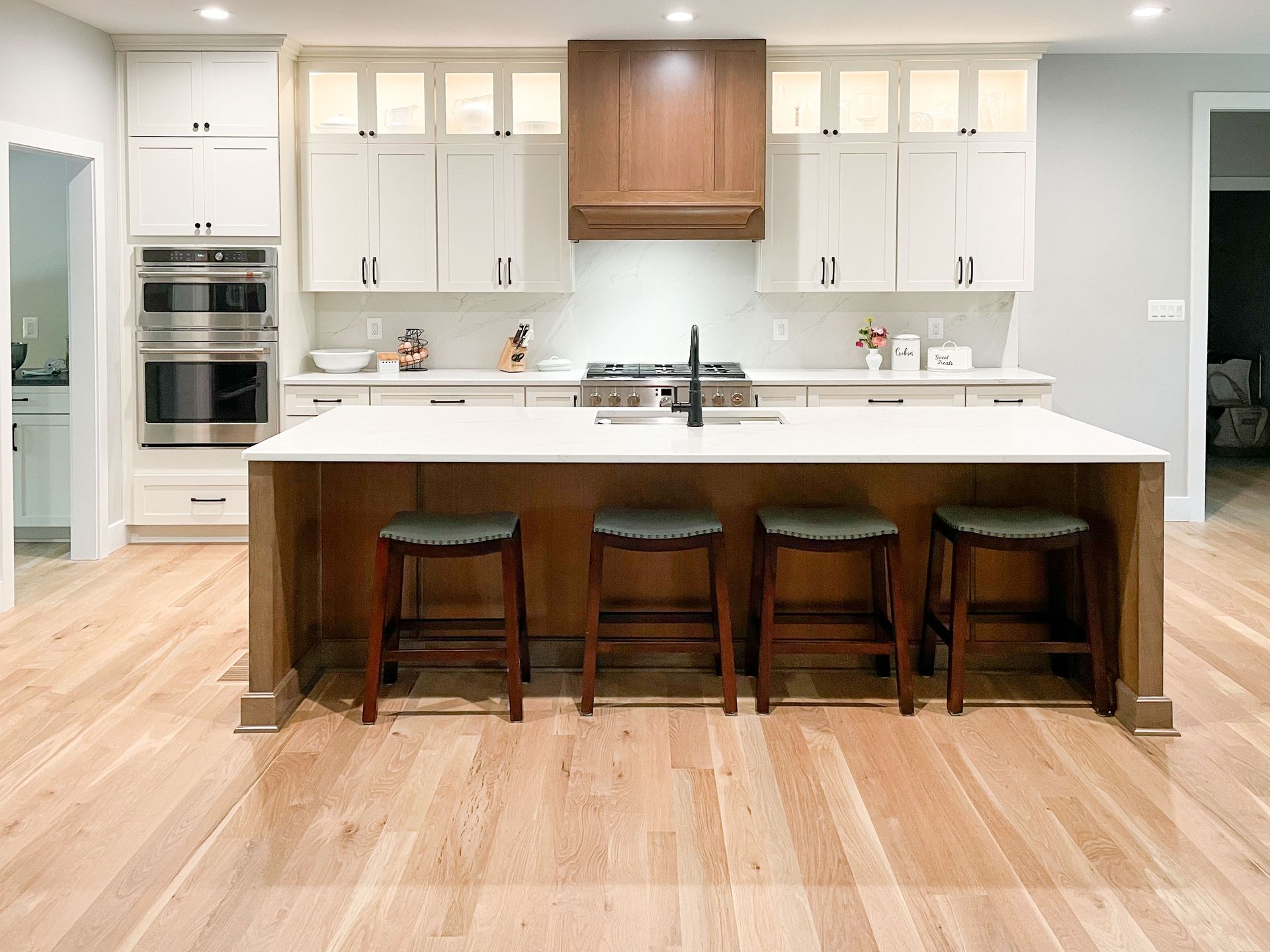 Kitchen with white cabinets, wooden island and floor, stools, and stainless steel appliances.