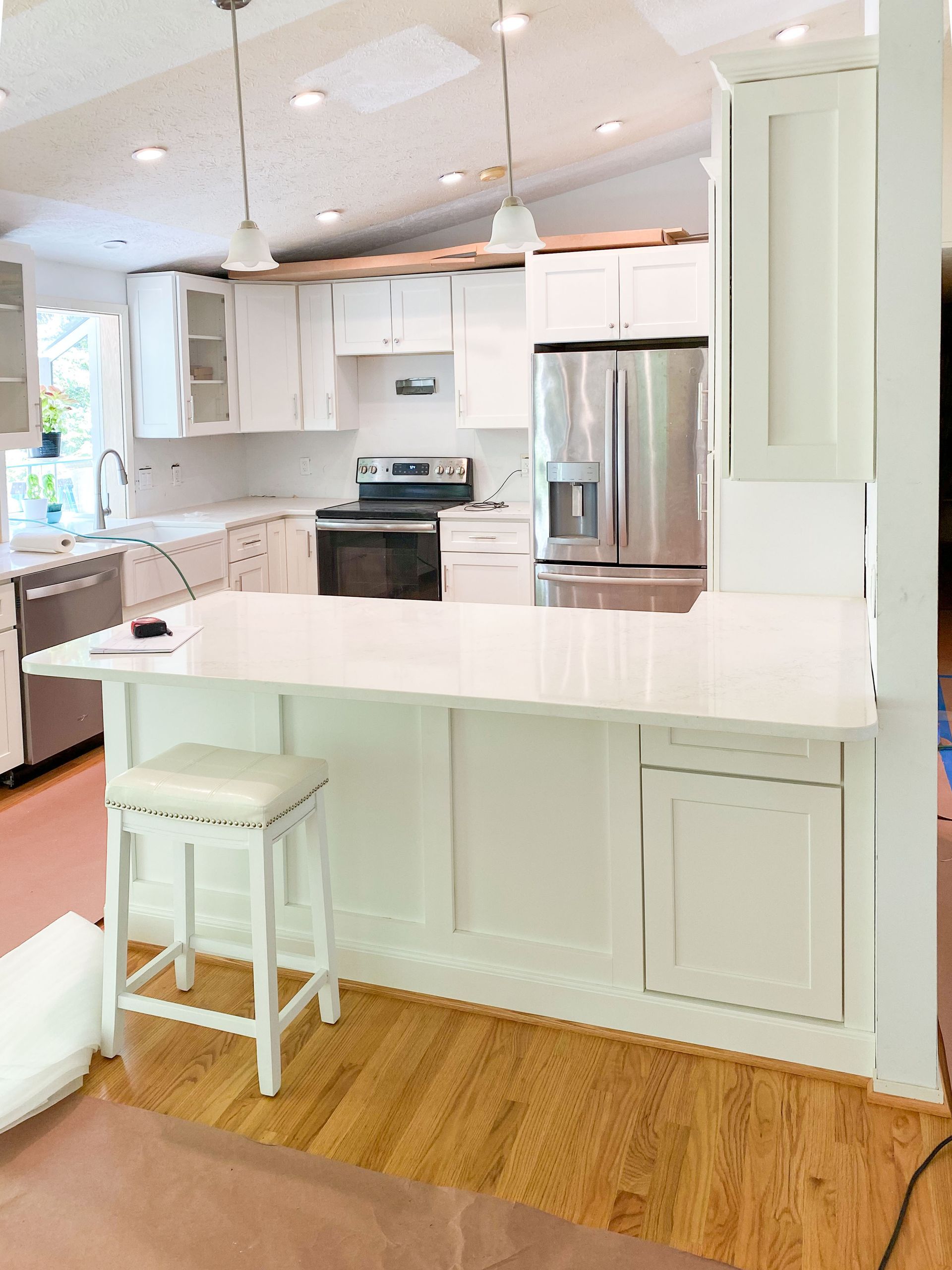 White kitchen with a countertop, cabinetry, and stainless steel refrigerator; a barstool is in front.