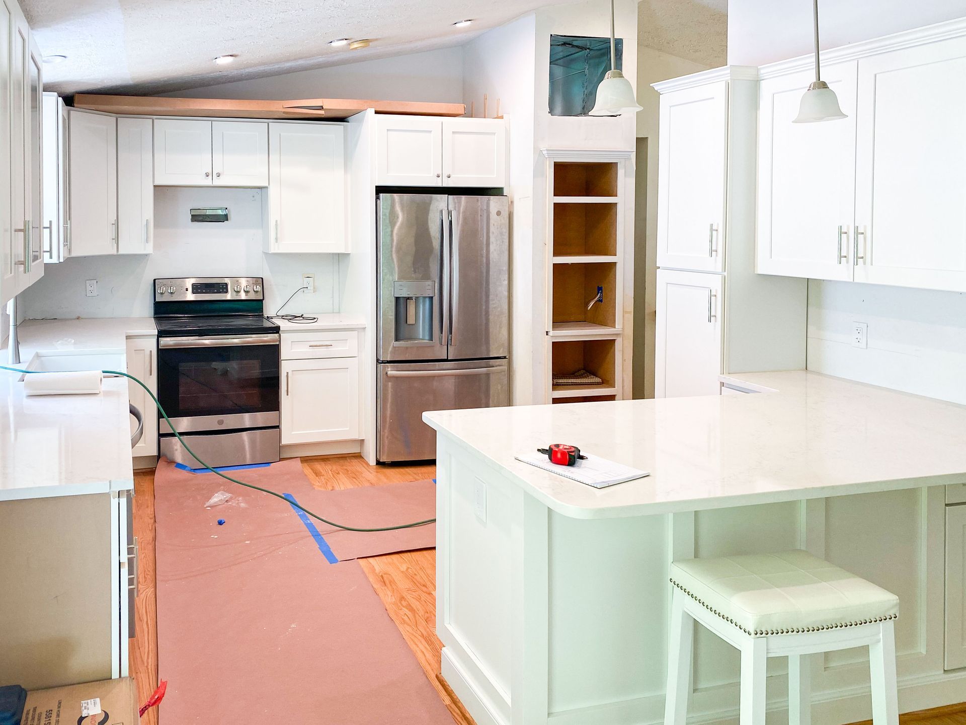 White kitchen under construction with white cabinets, stainless steel appliances, and island.