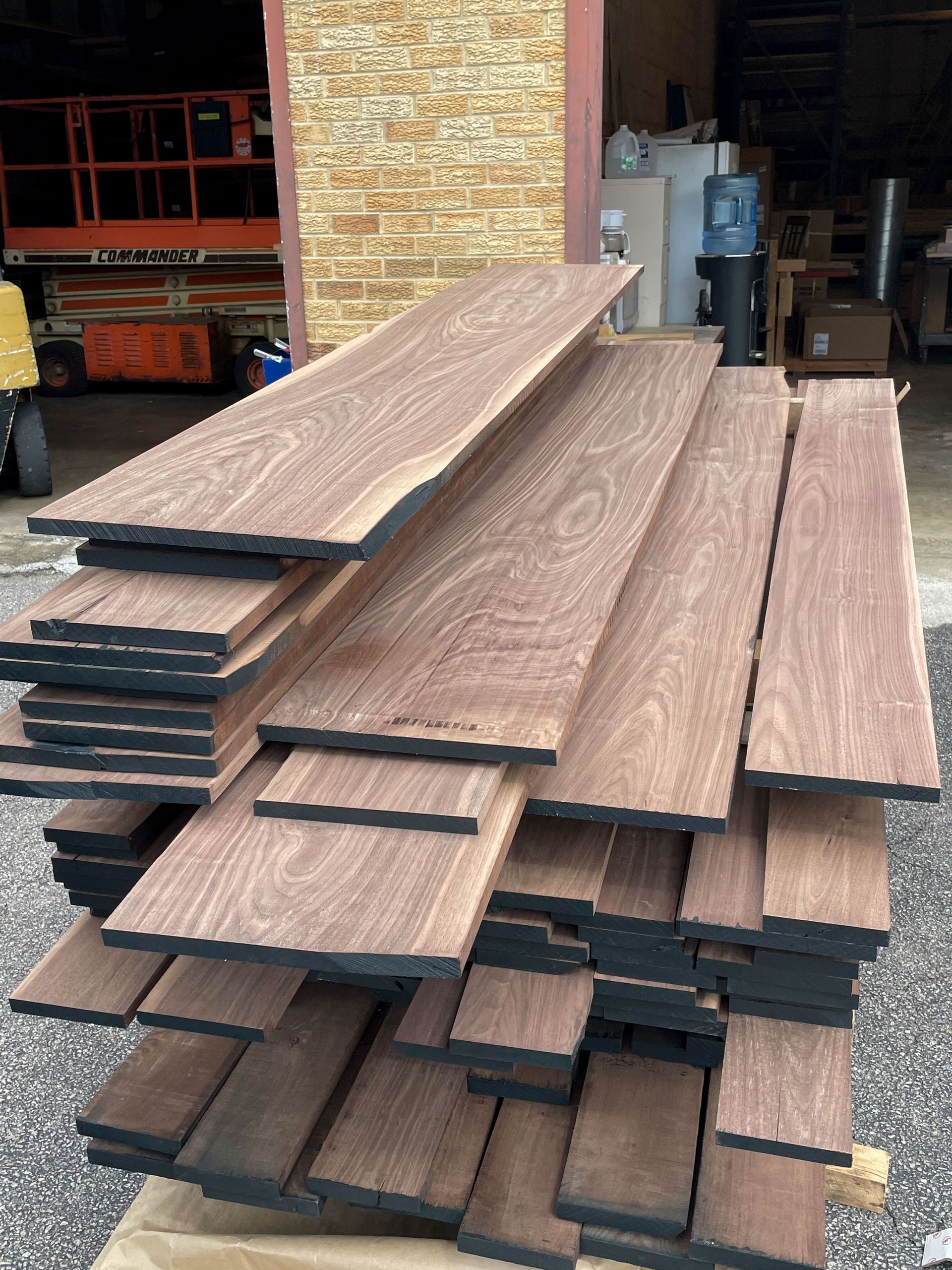 Stack of dark wood planks, possibly lumber, in a warehouse setting.