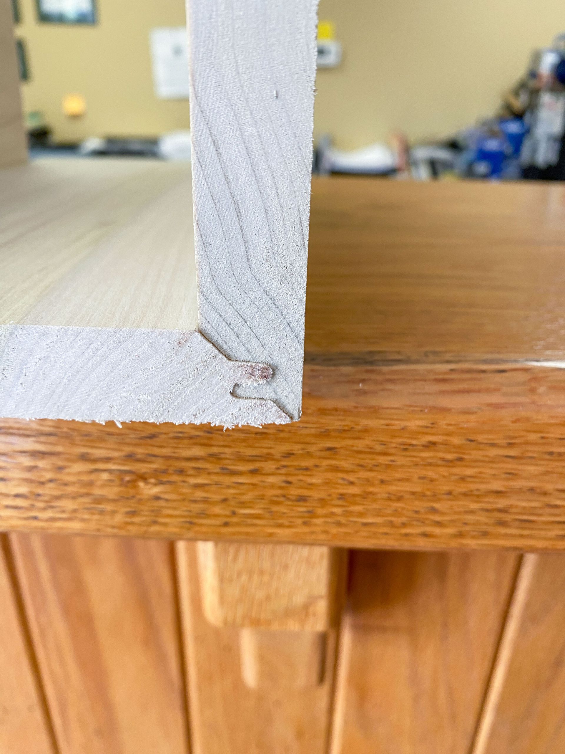 Close-up of a light-colored wooden frame stapled to a darker wood surface.