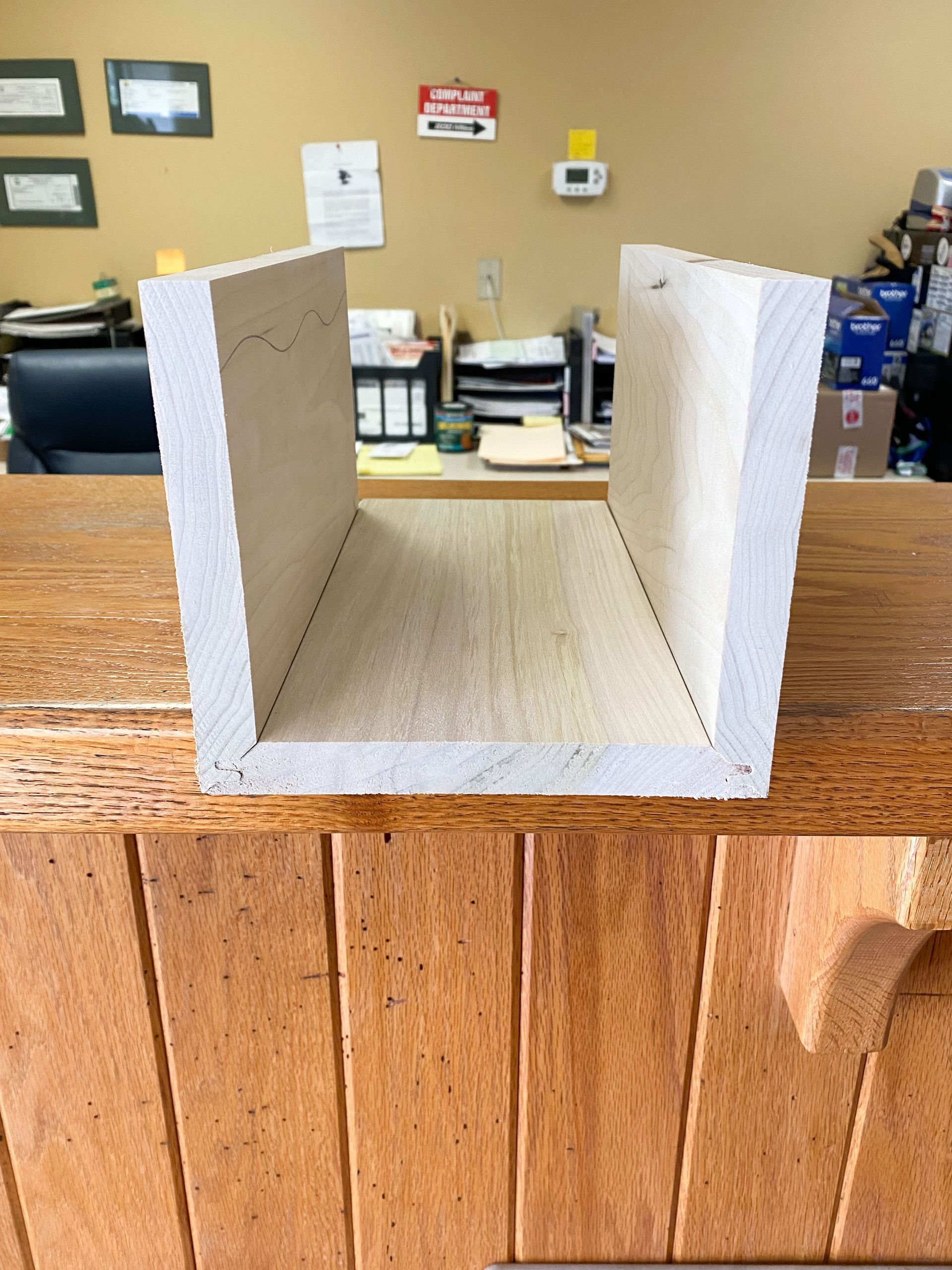 Wooden U-shaped structure, light wood interior, resting on a darker wooden surface in an office.